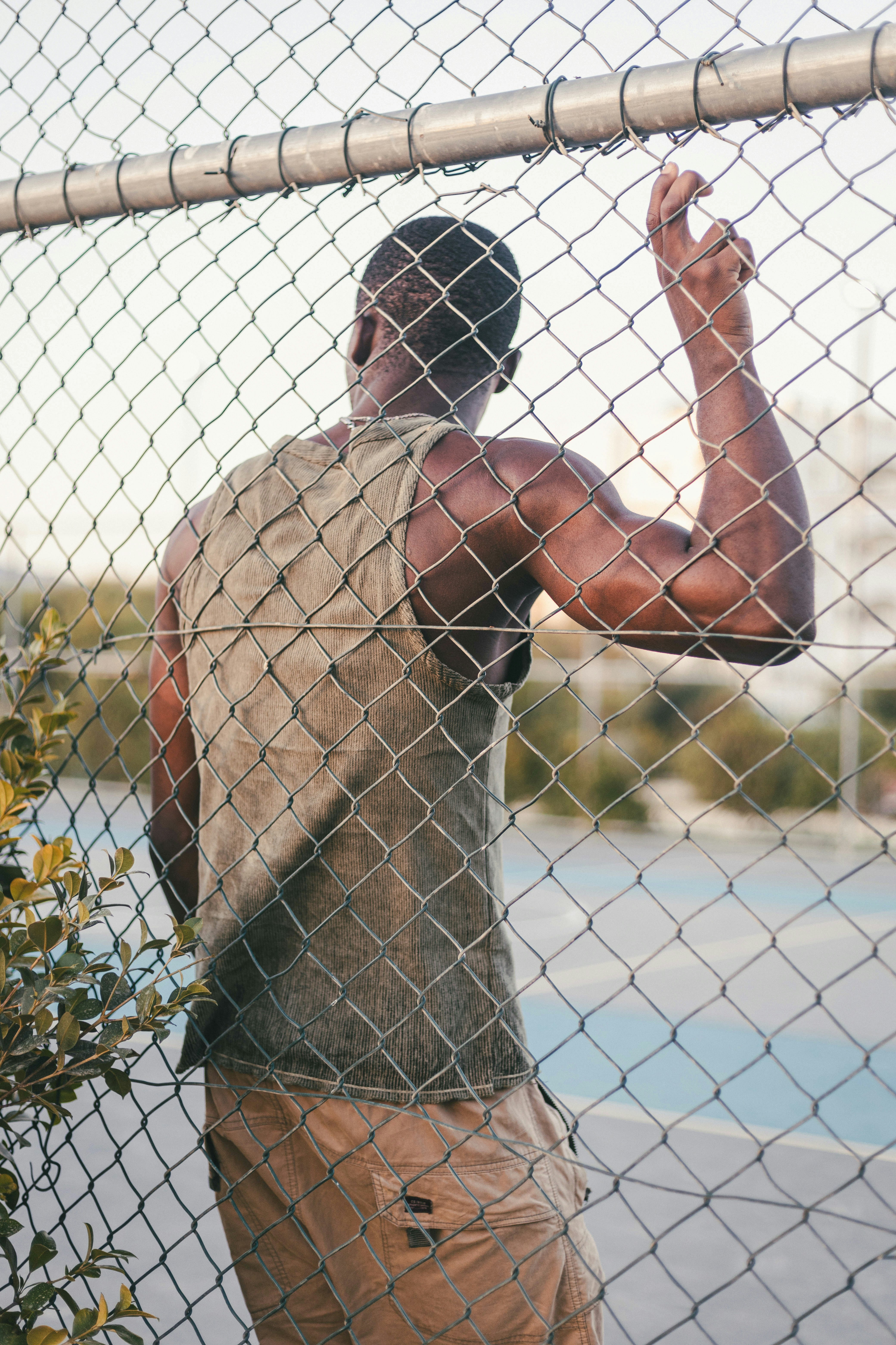 Muscular man leaning against a chain-link fence