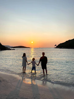 Family holding hands in water at sunset