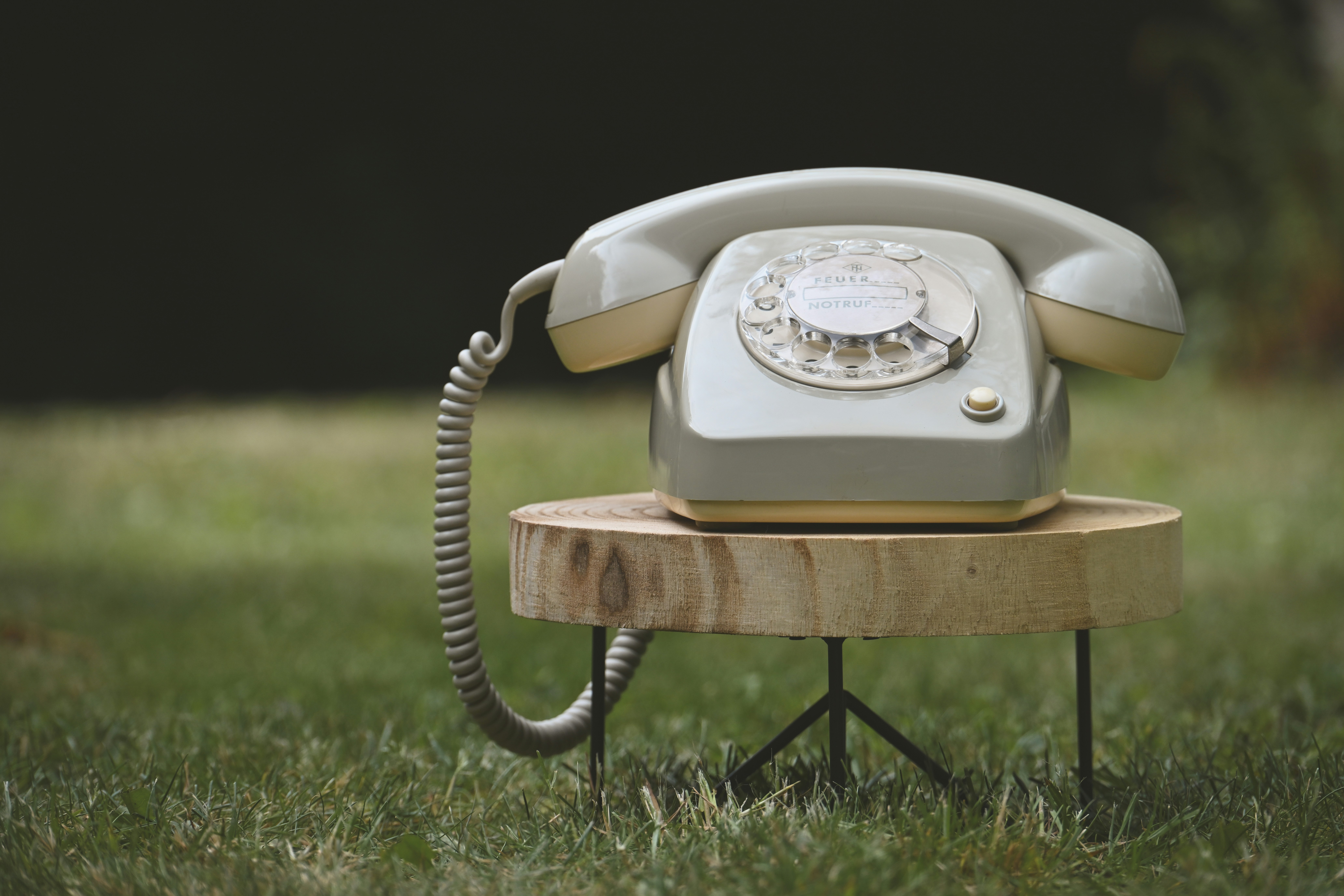 Telefone rotativo antigo em um banquinho de madeira na grama verde.