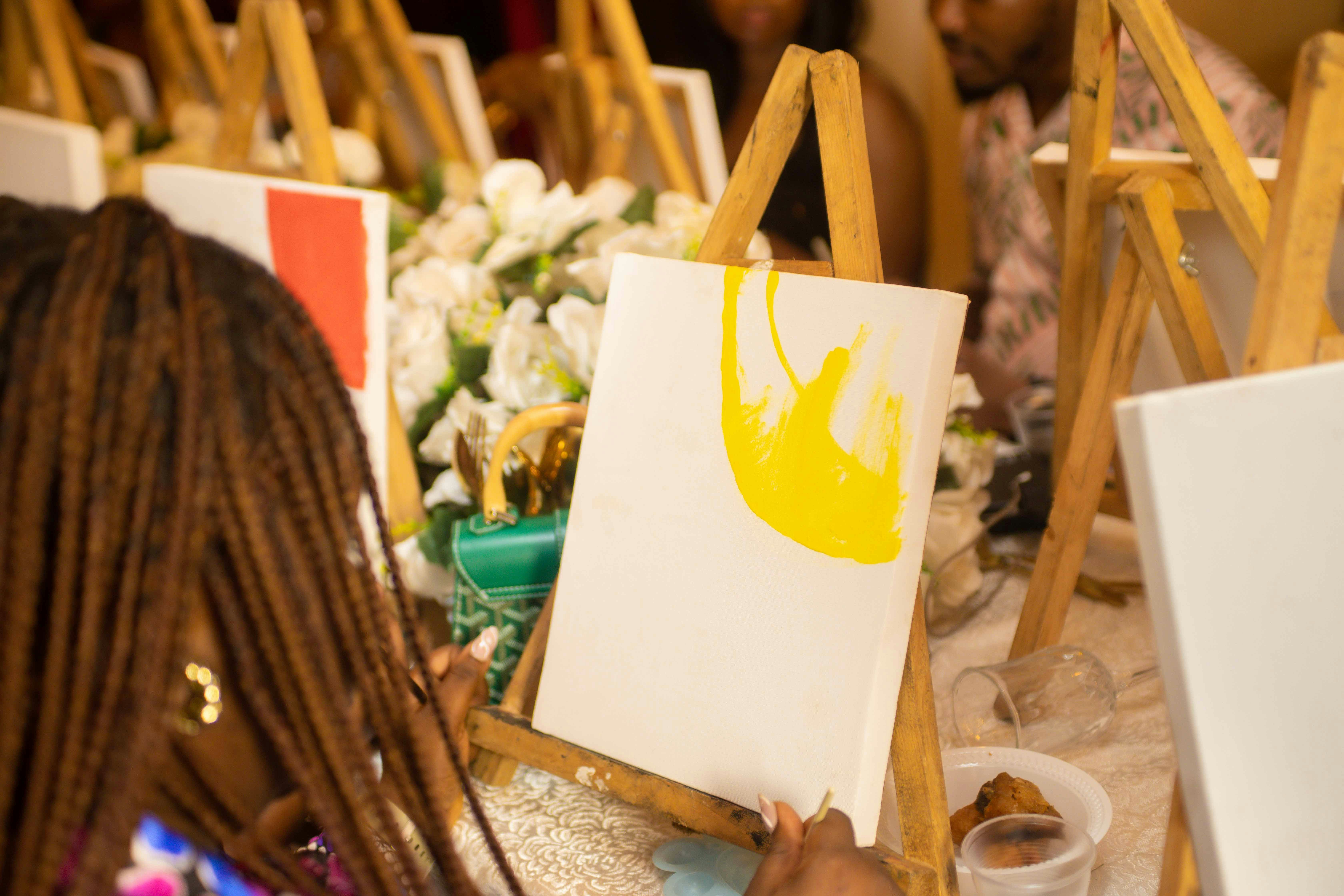 Someone painting yellow on a canvas at an art class.