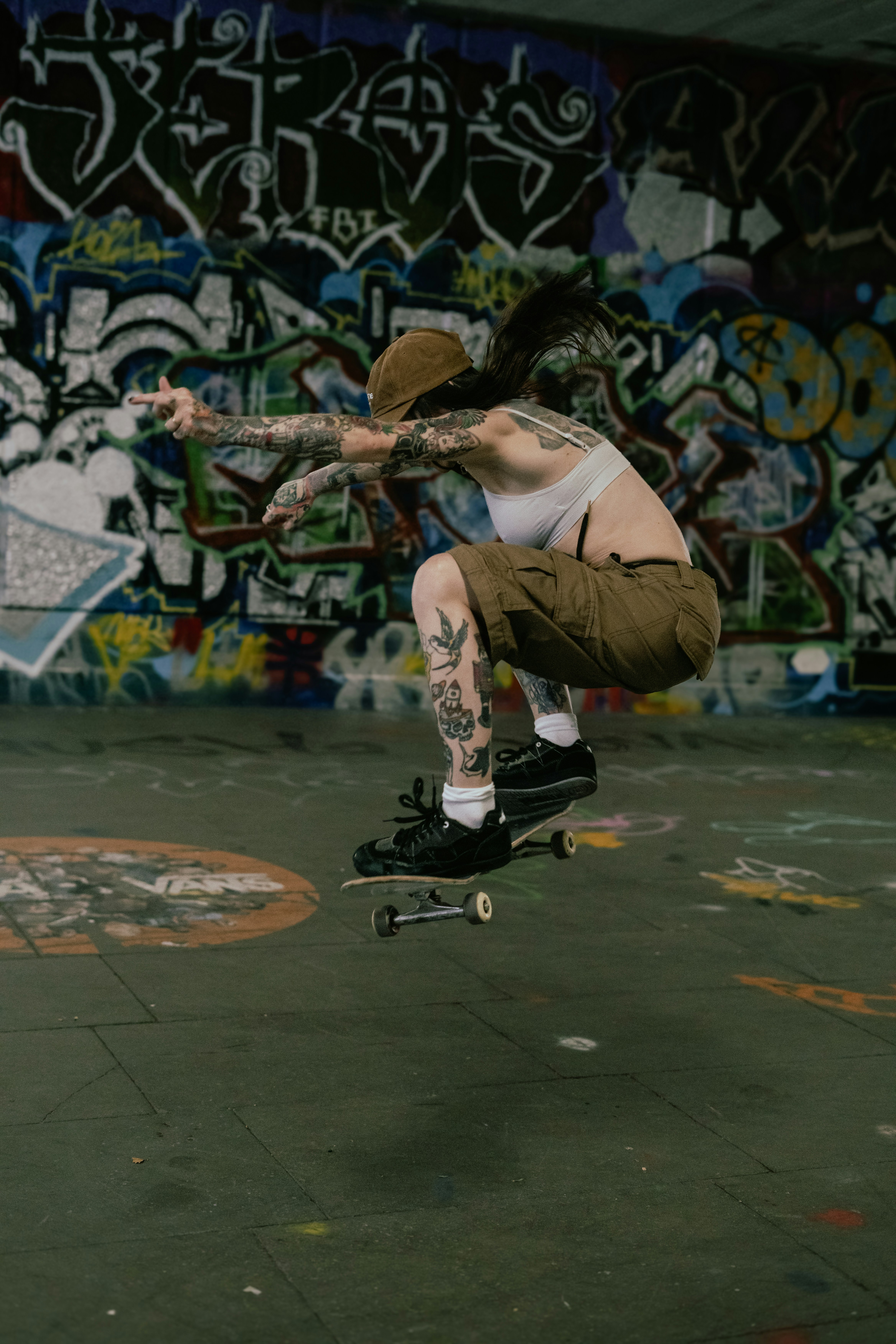 Tattooed person skateboarding in mid-air against graffiti wall