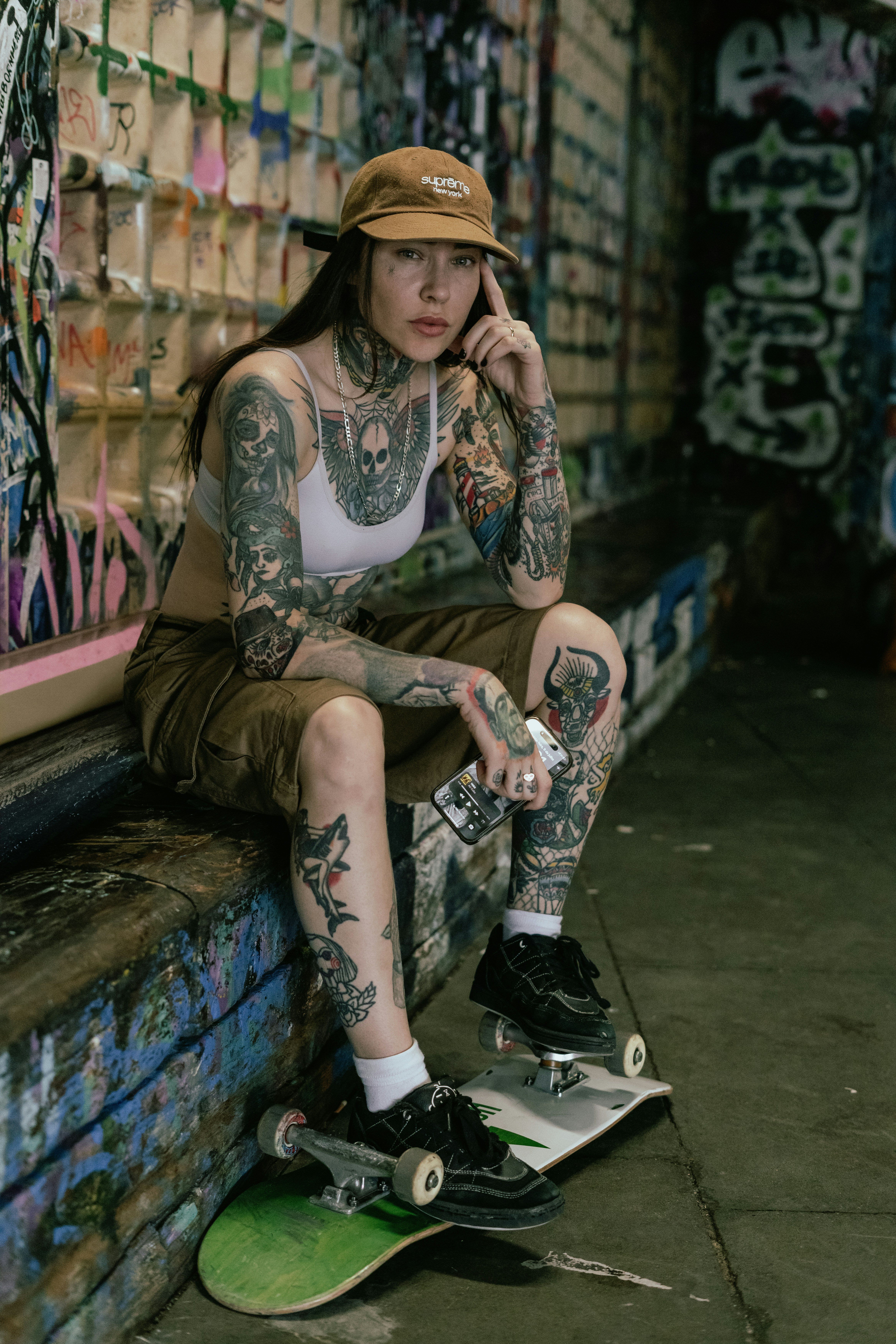 Tattooed woman in a cap sitting by a skateboard