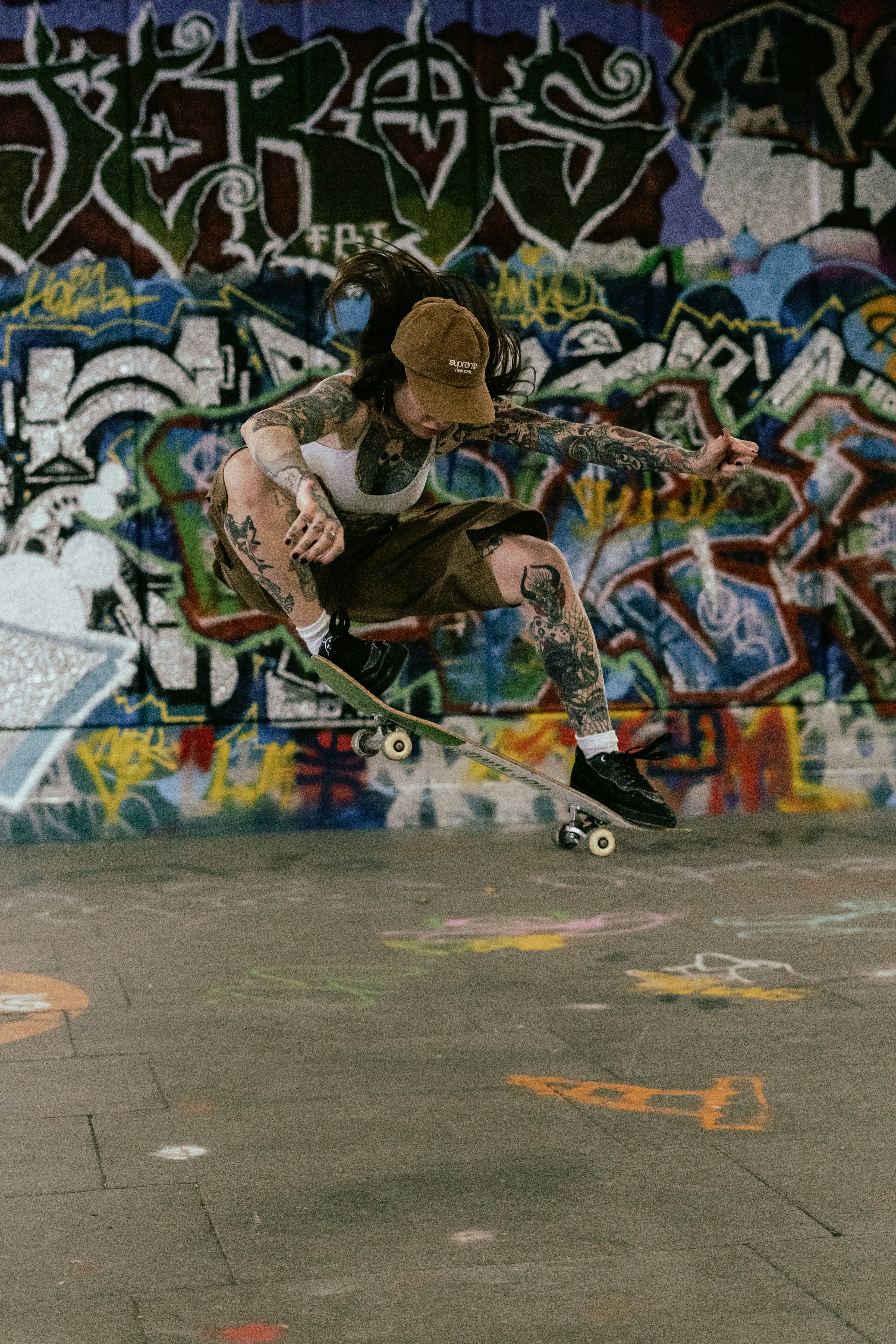 Tattooed person skateboarding mid-air in front of graffiti