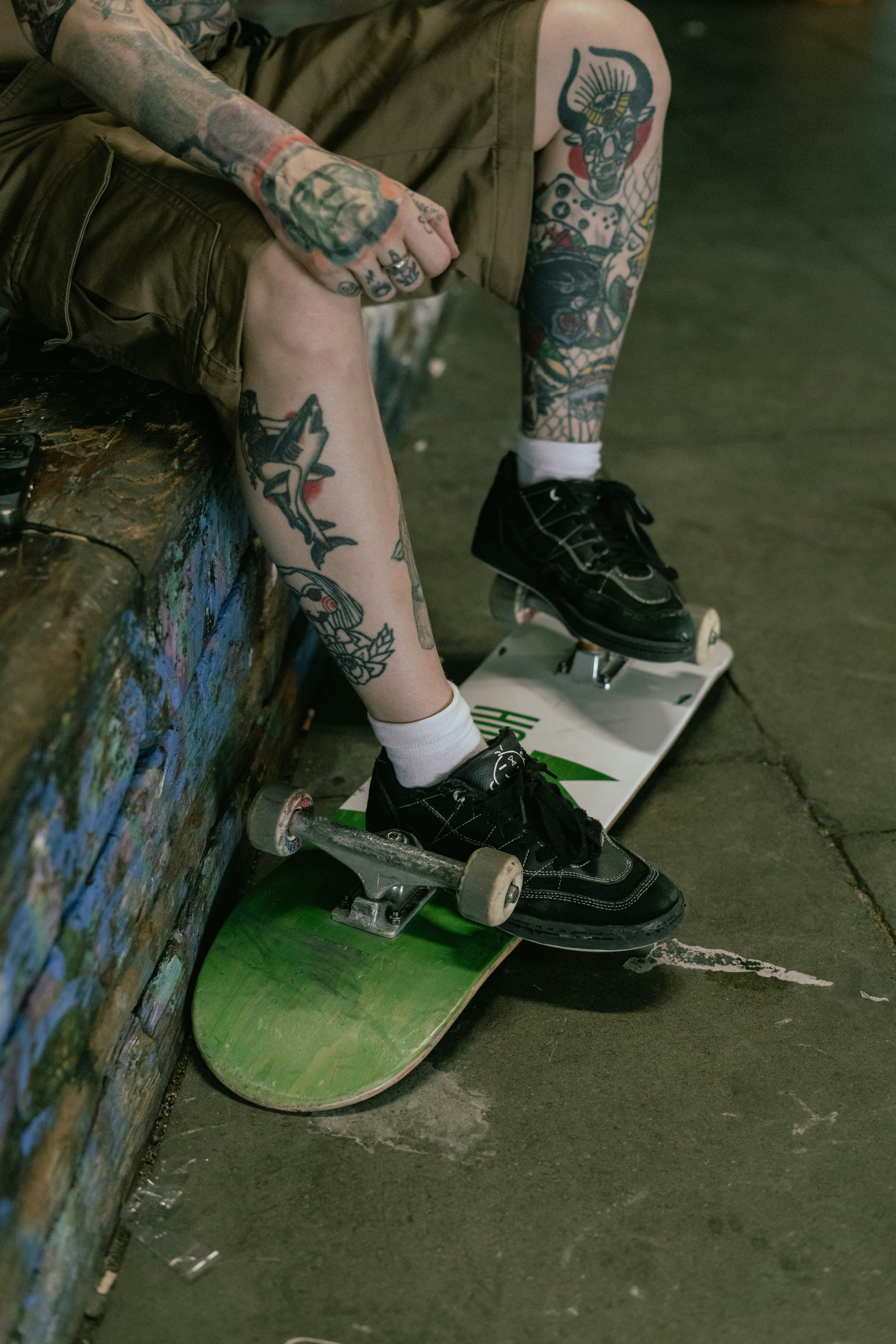 Tattooed person sitting on a ledge with a skateboard