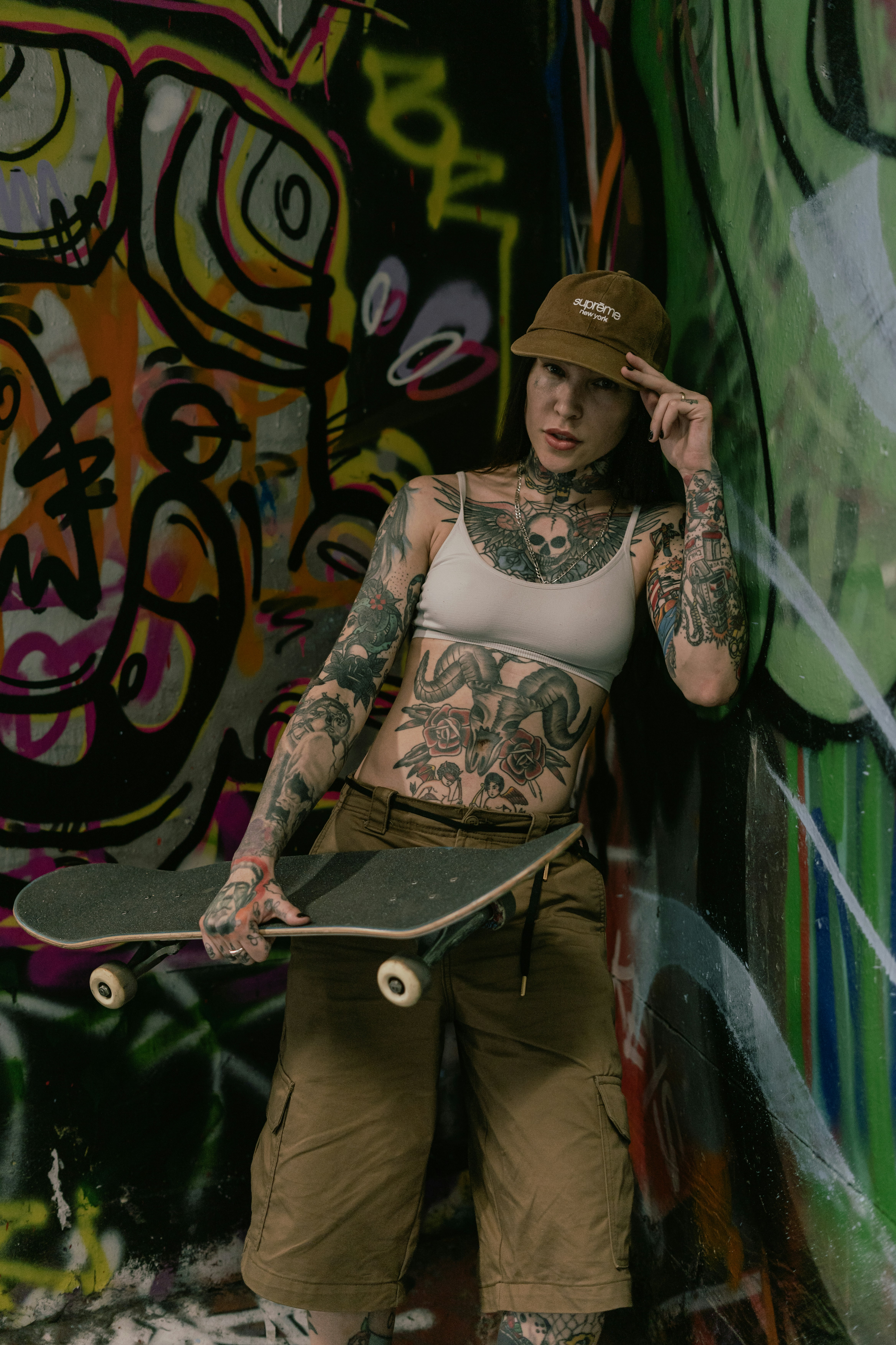 Tattooed person holding a skateboard against a colorful graffiti background
