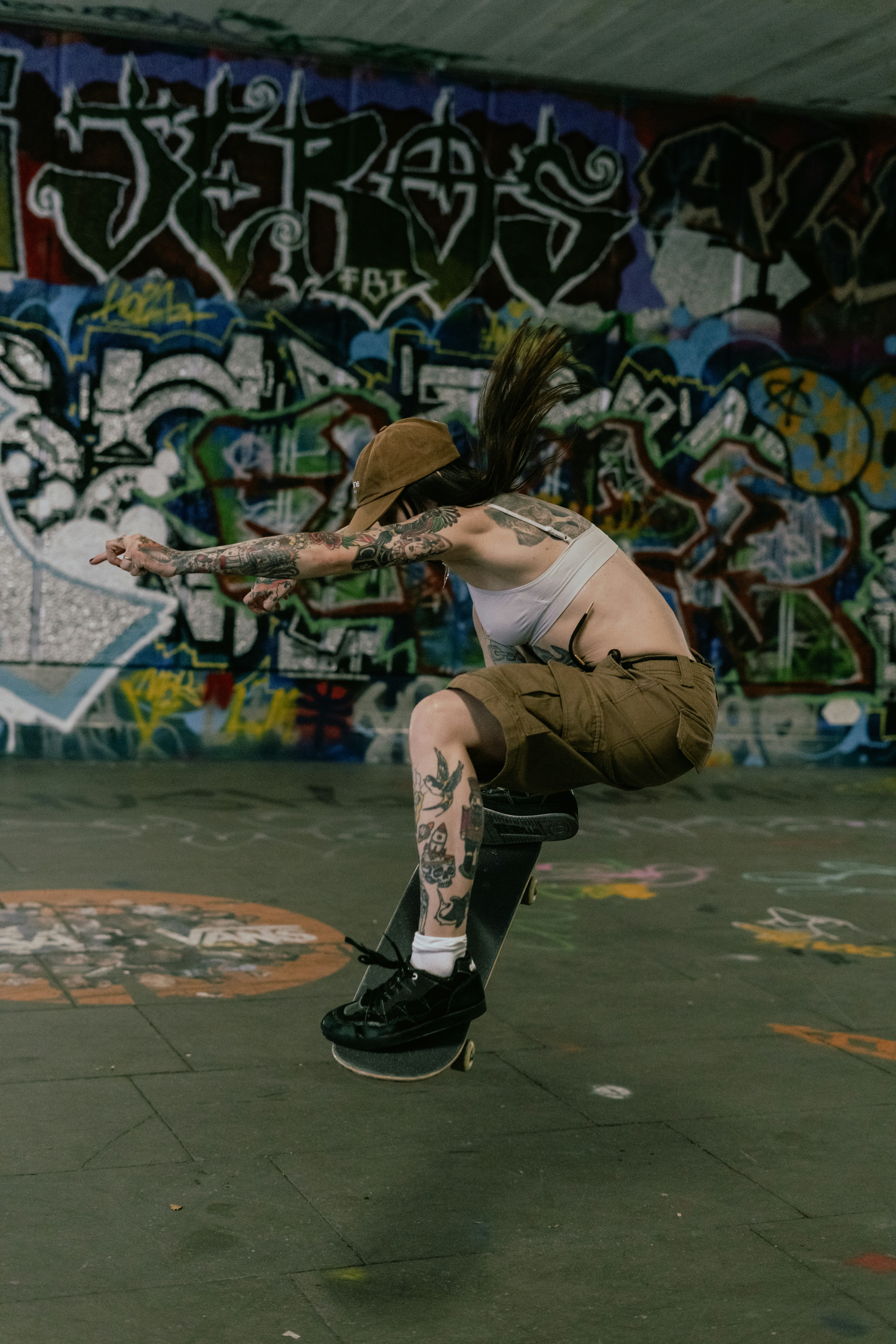 Tattooed woman skateboarding mid-air in an urban skatepark