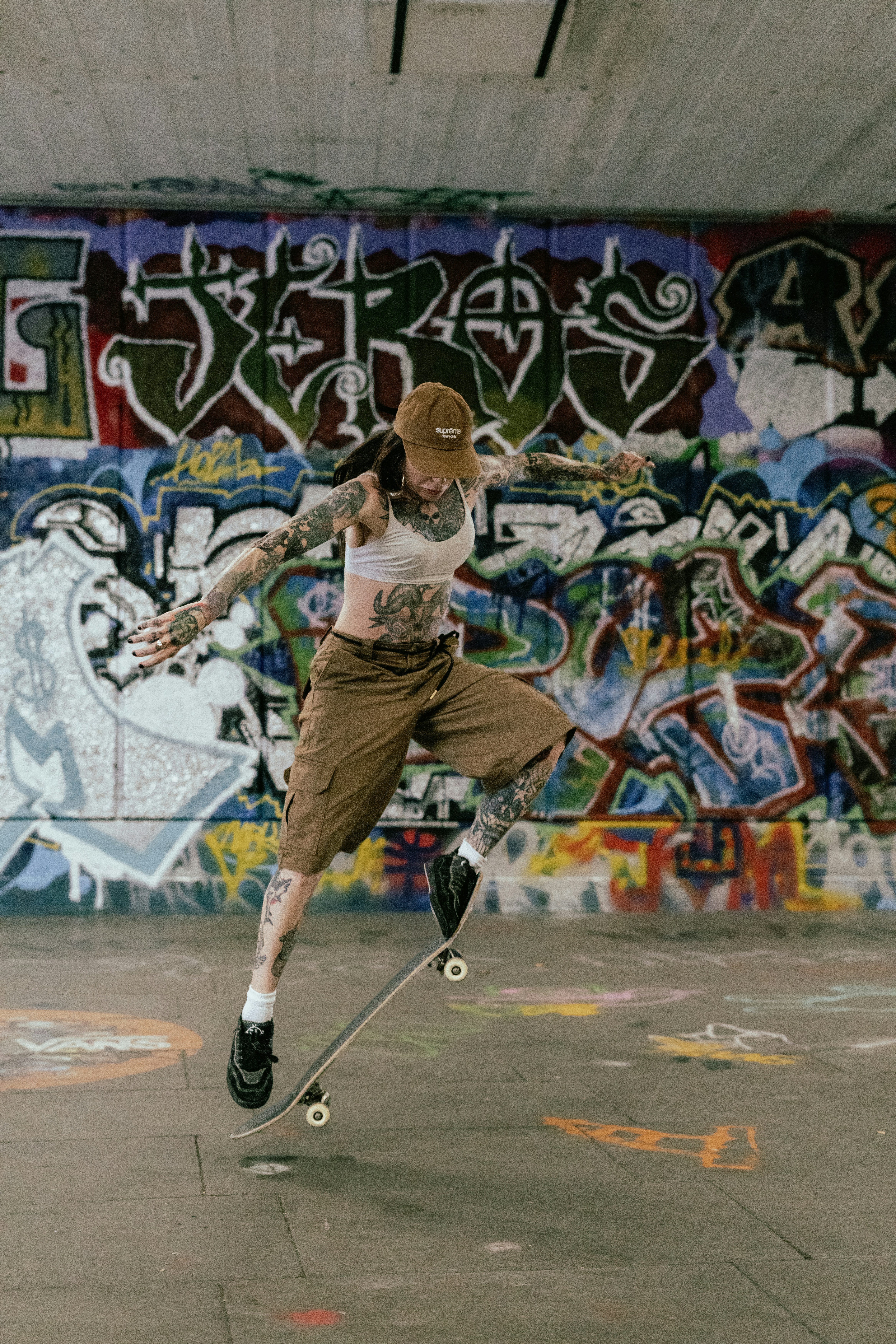 A tattooed person skateboarding mid-air against a graffiti wall
