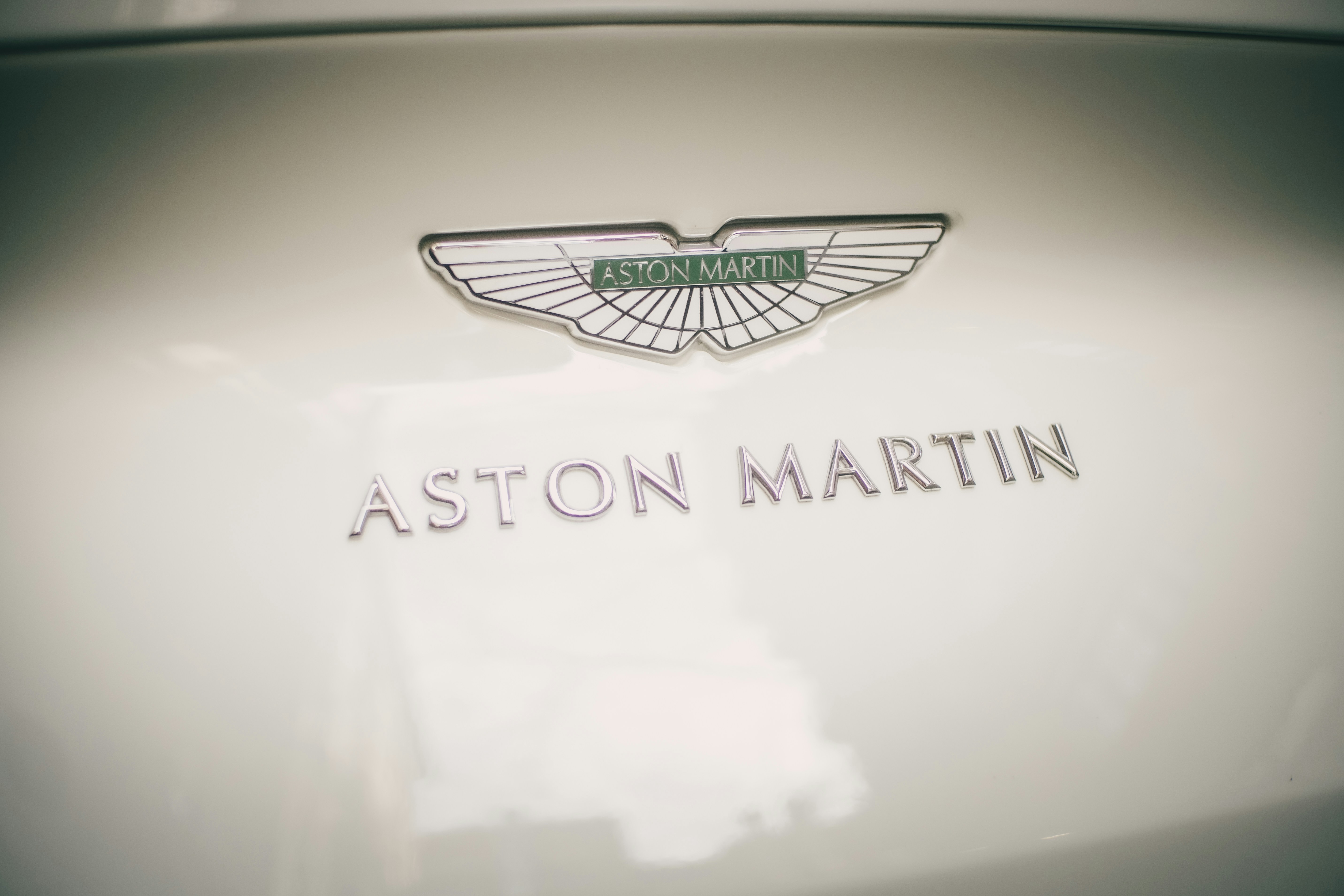 Logo et texte ailés d’Aston Martin sur une surface blanche.