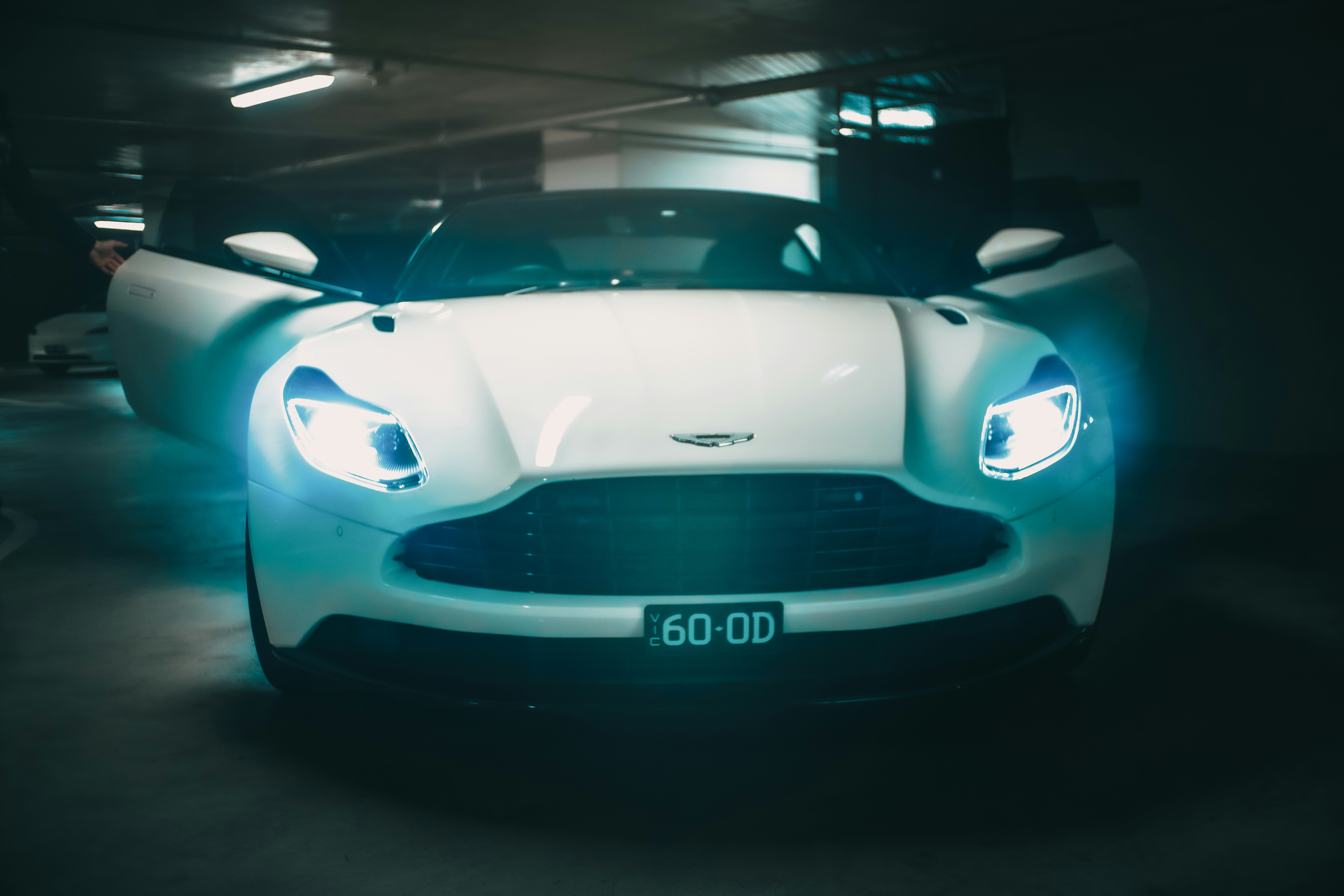 White luxury car with glowing headlights in a dark garage.