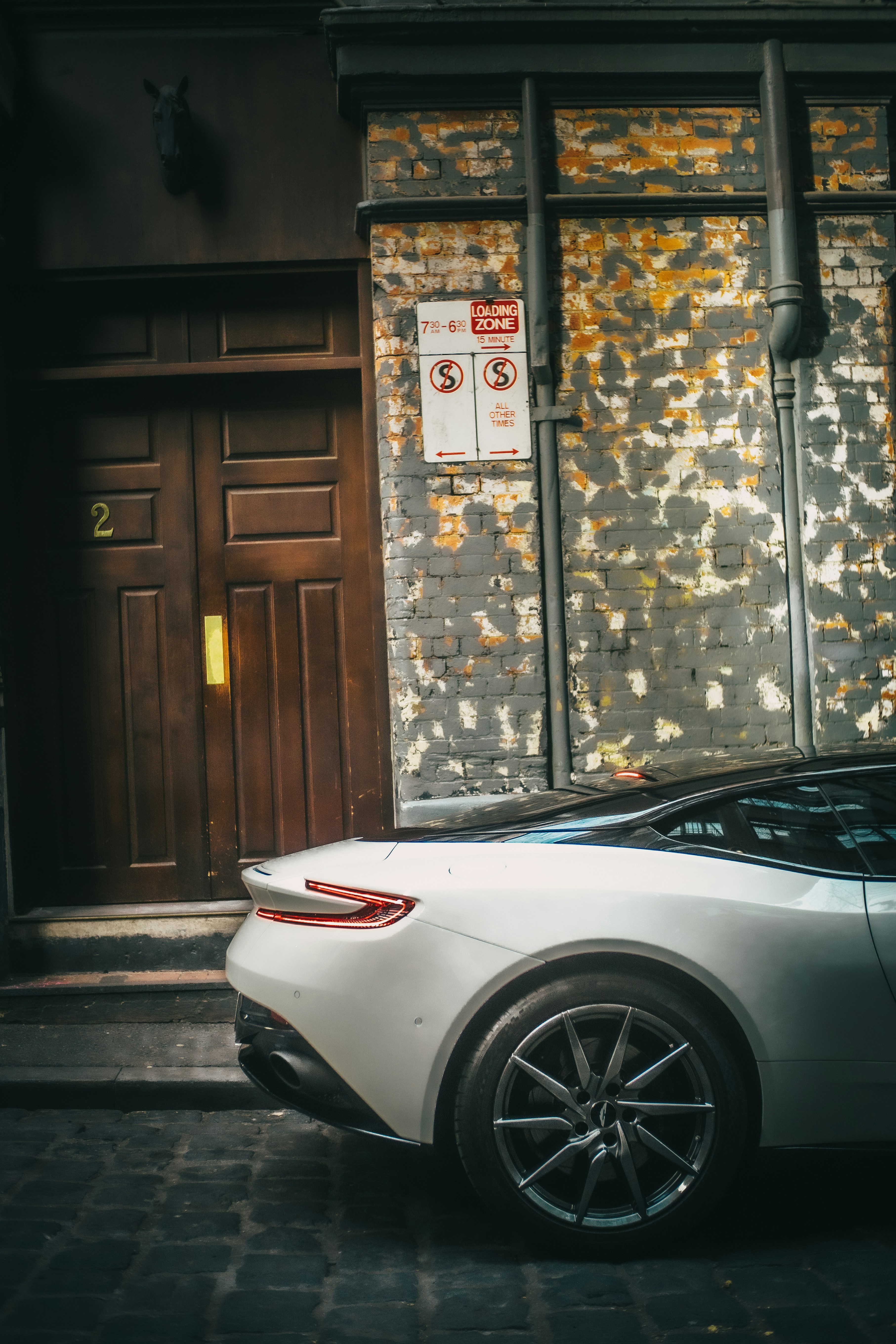Voiture de sport blanche de luxe garée près d’un vieux mur de briques.