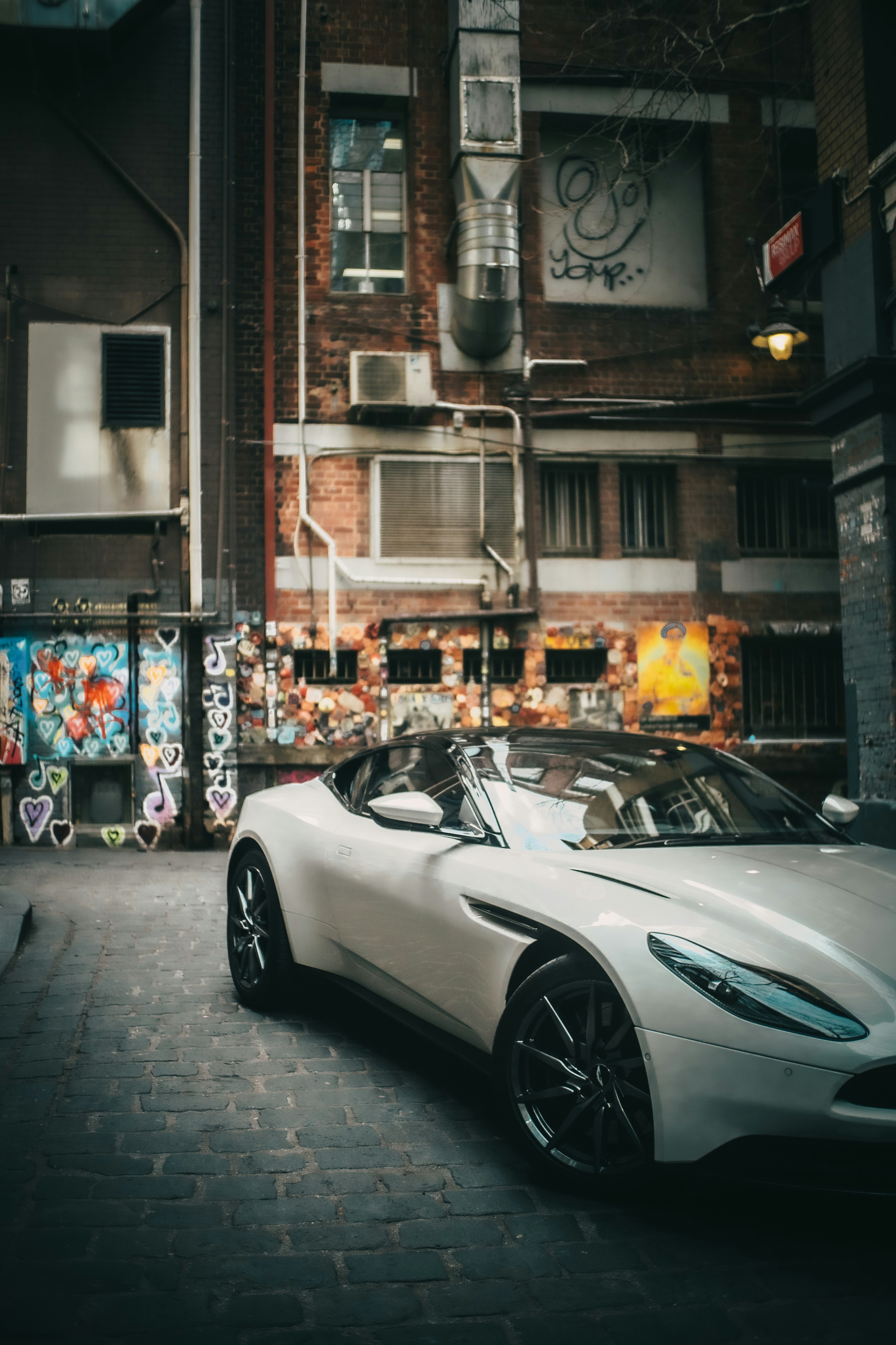 Voiture de sport de luxe blanche garée dans une ruelle urbaine couverte de graffitis.