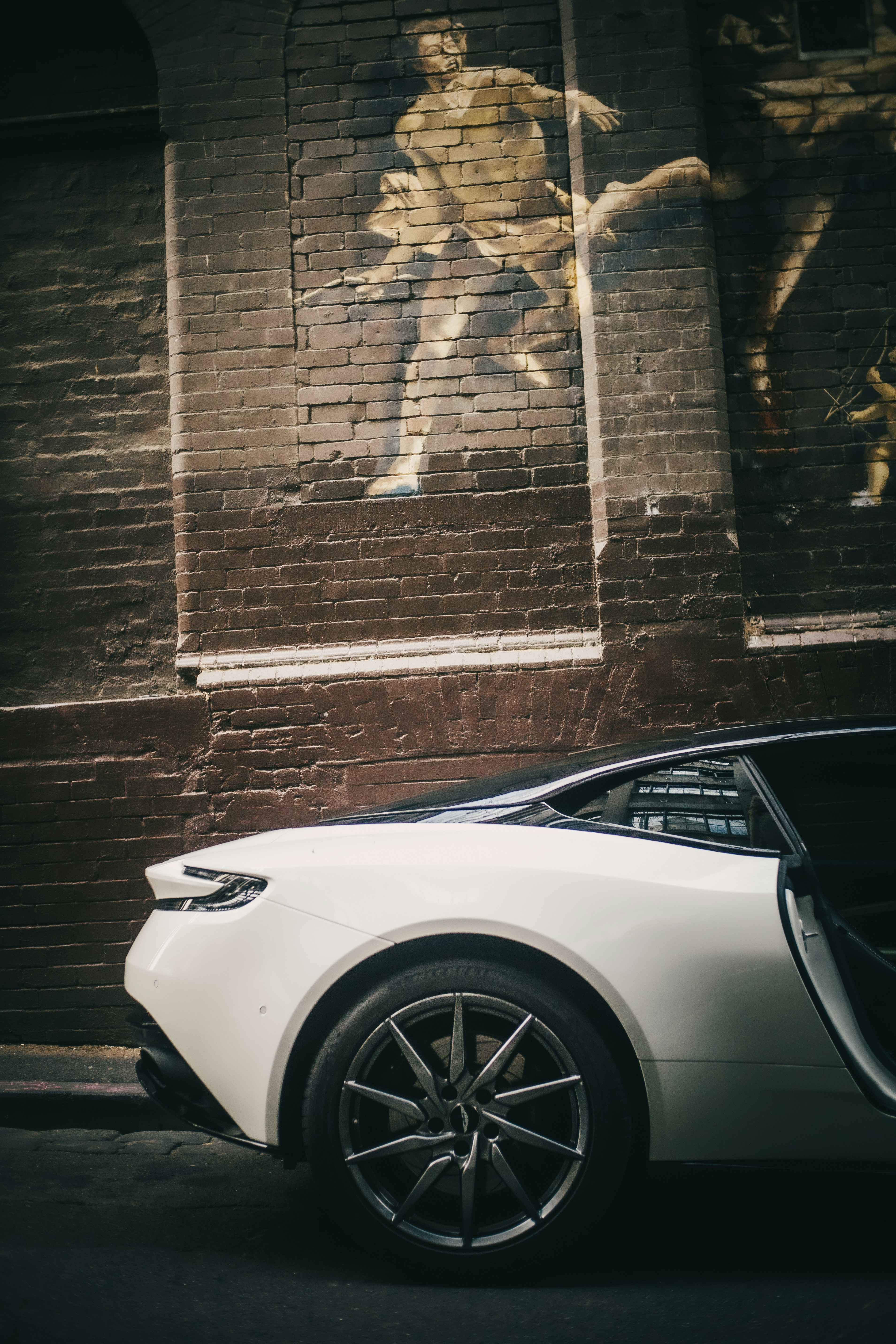 Voiture de sport blanche garée contre une fresque murale en briques.