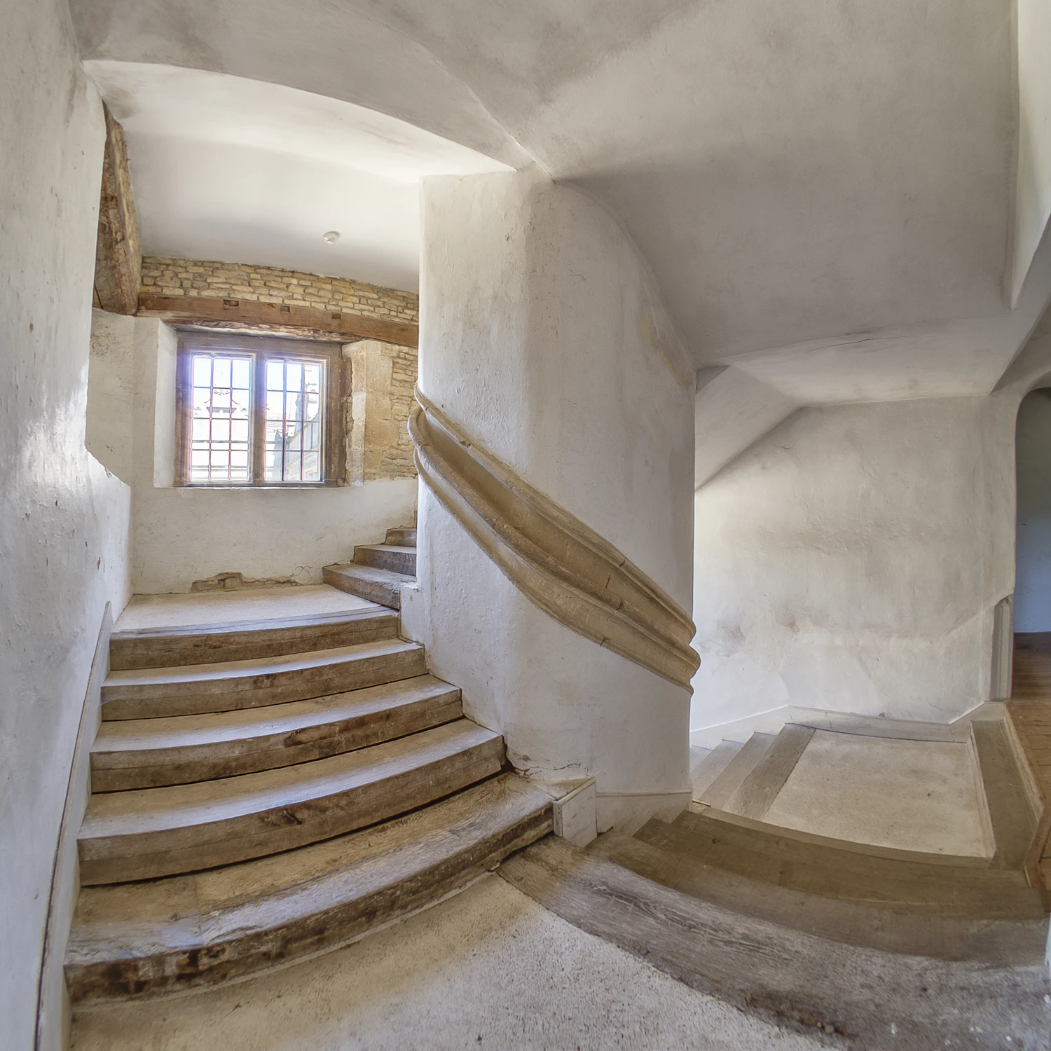 A whitewashed stone staircase curving past a small barred window