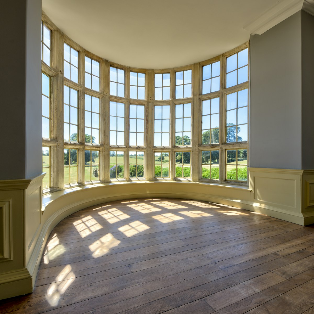 Sunlight streaming through large curved windows onto a wood floor