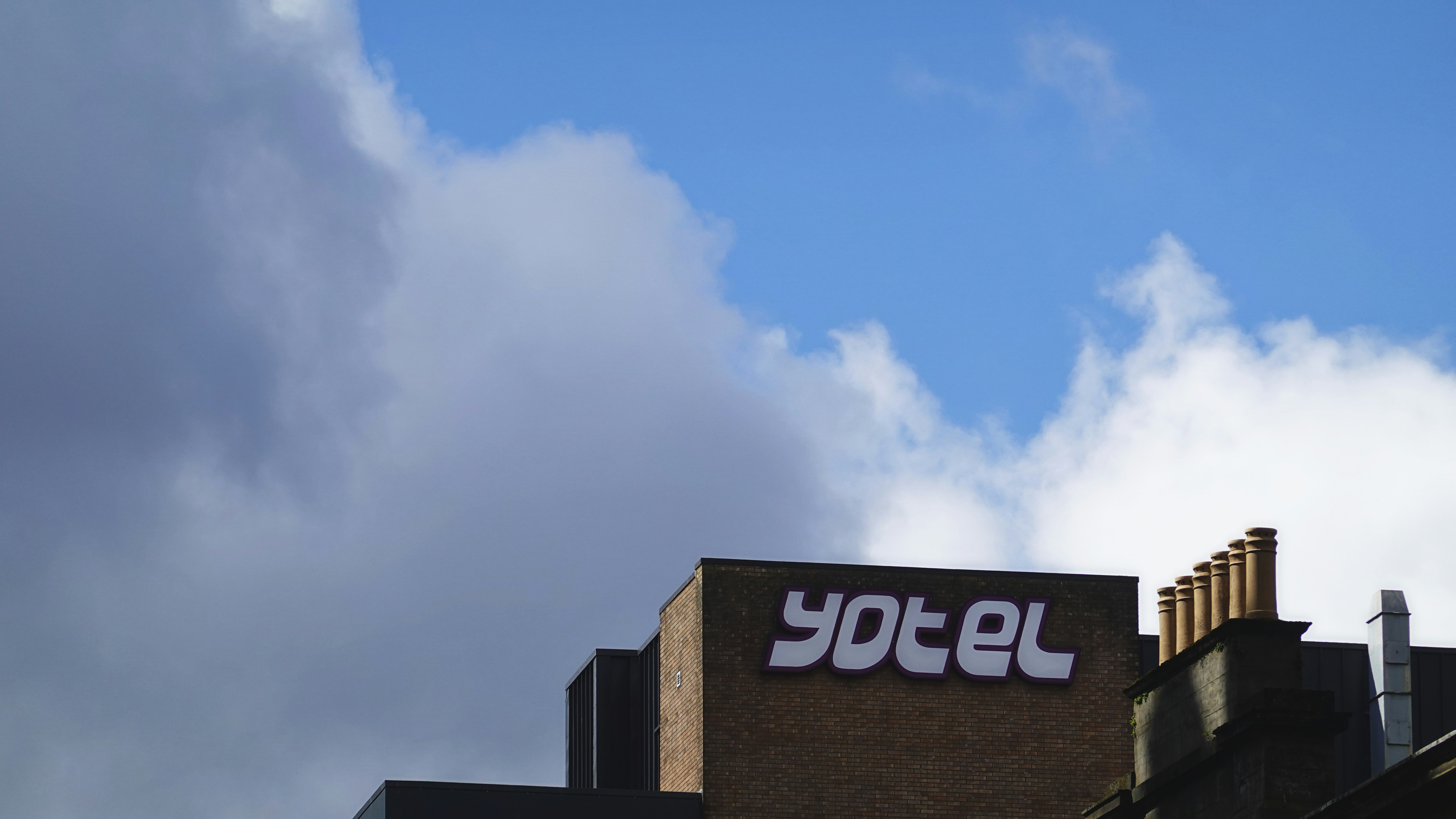 Cartello Yotel su un edificio contro un cielo azzurro nuvoloso.