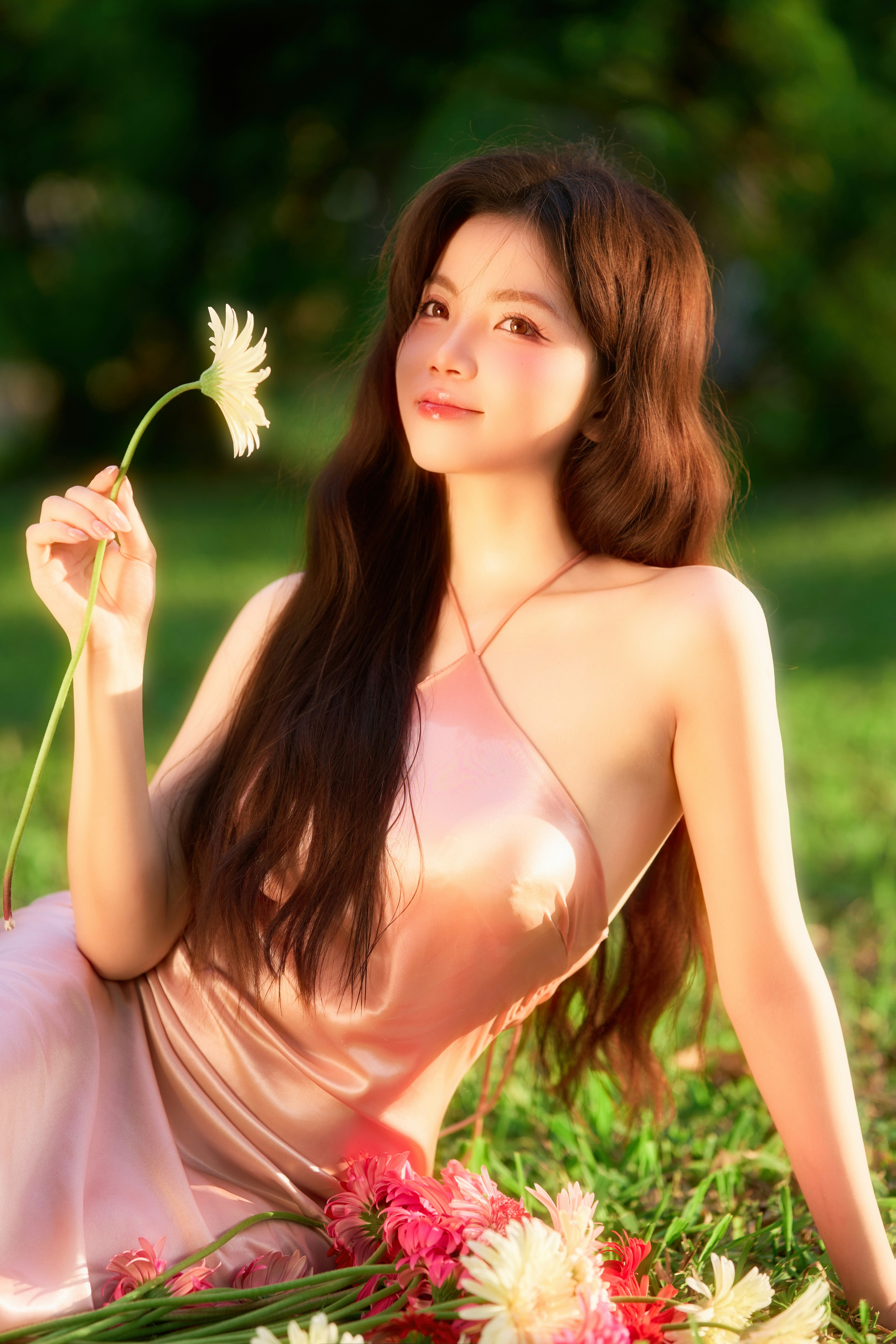 Beautiful woman in pink dress holding flower on green grass.