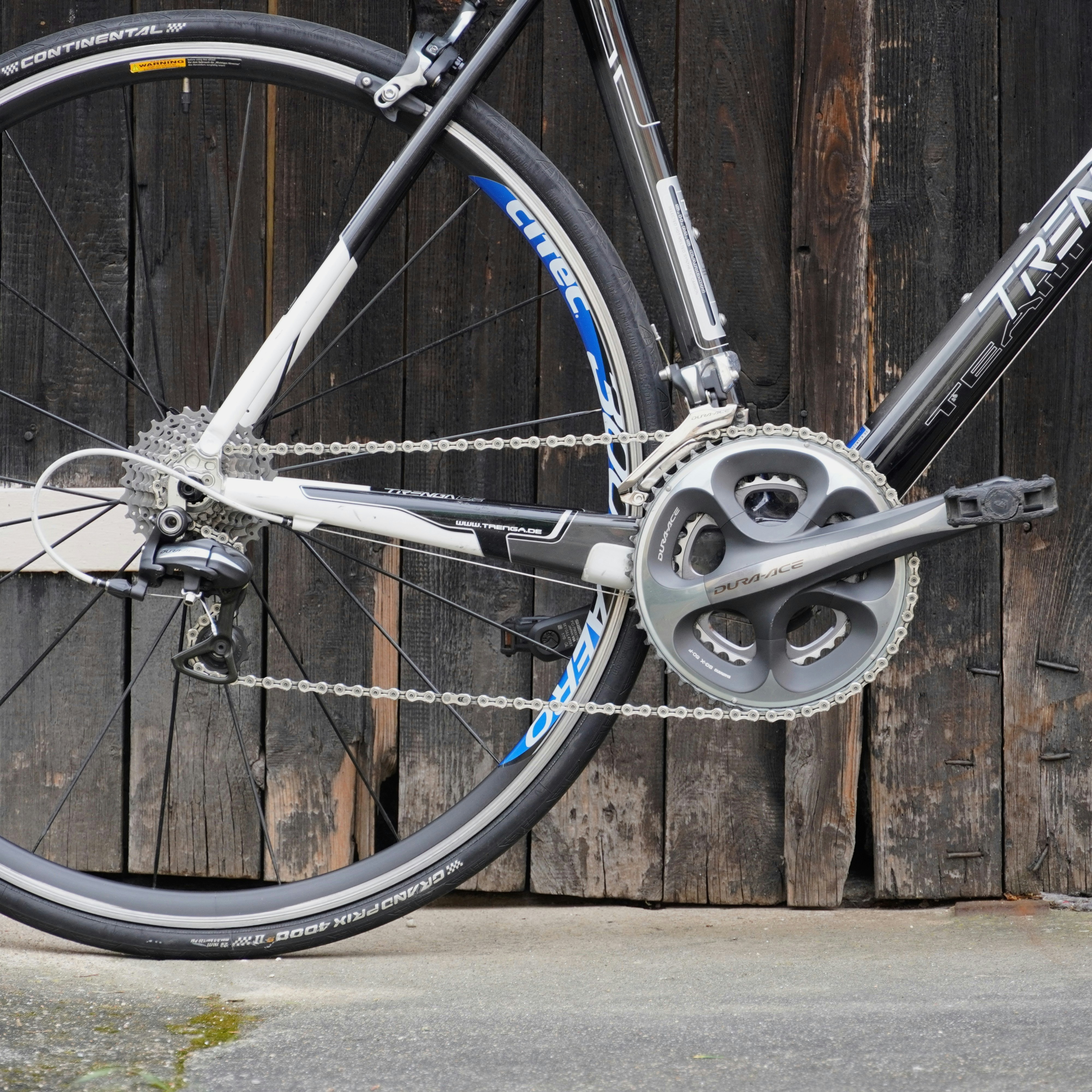 A bicycle's rear wheel and gears against a wooden wall