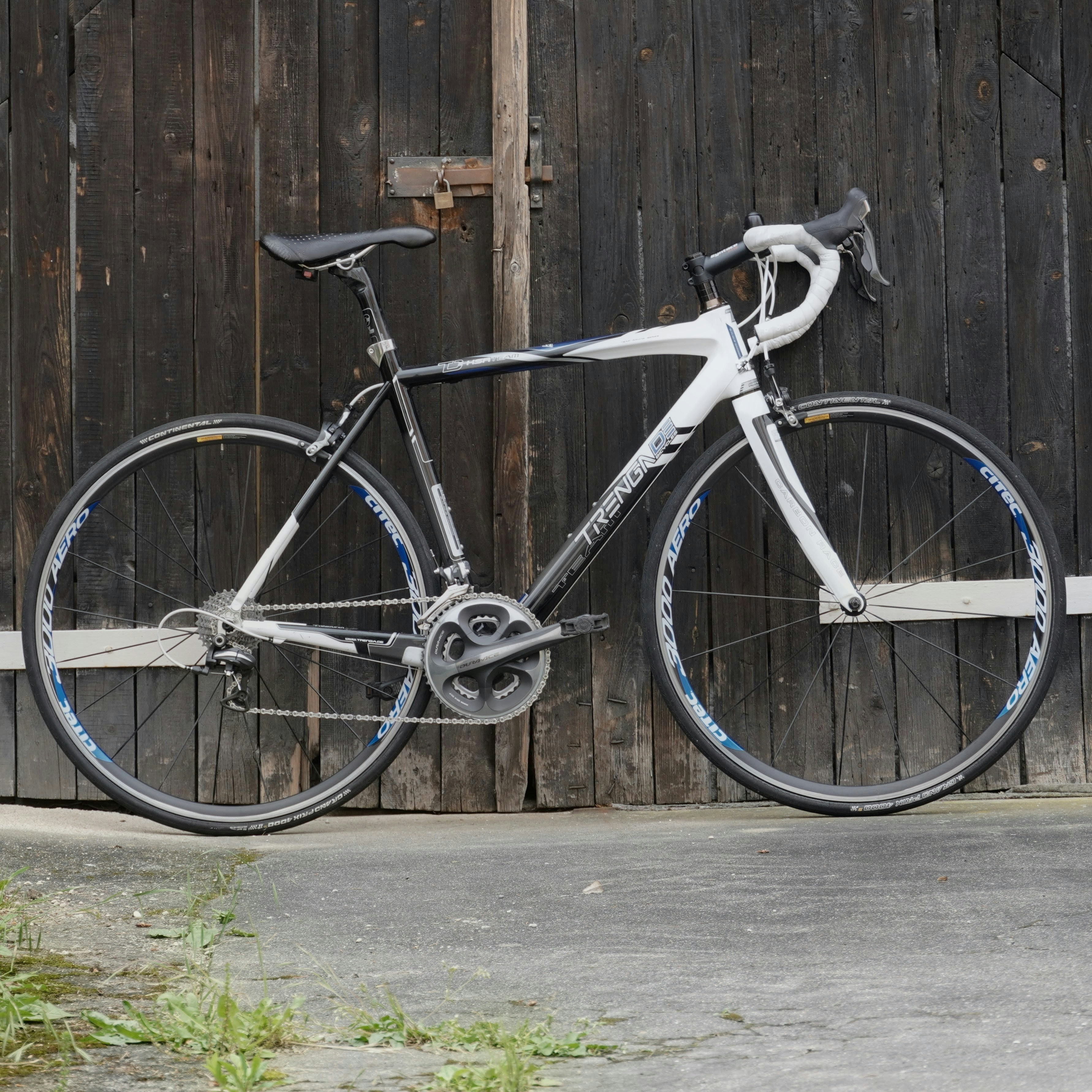 A road bicycle with white handlebars against a dark wooden barn door