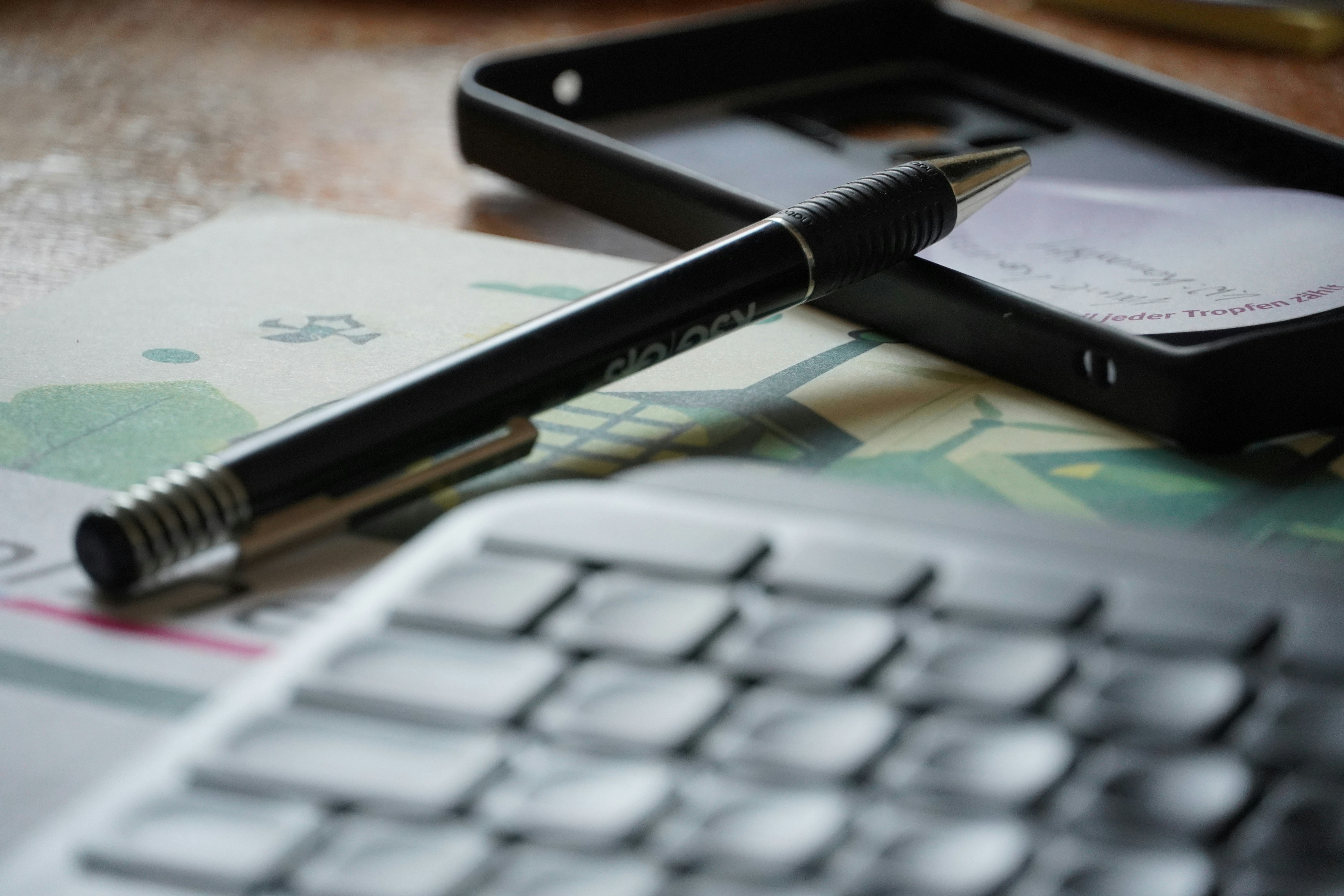 A black pen, phone case, and keyboard on a desk
