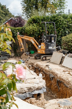 A mini excavator parked next to an open trench in a residential yard, the kind of dig a buried service line repair requires