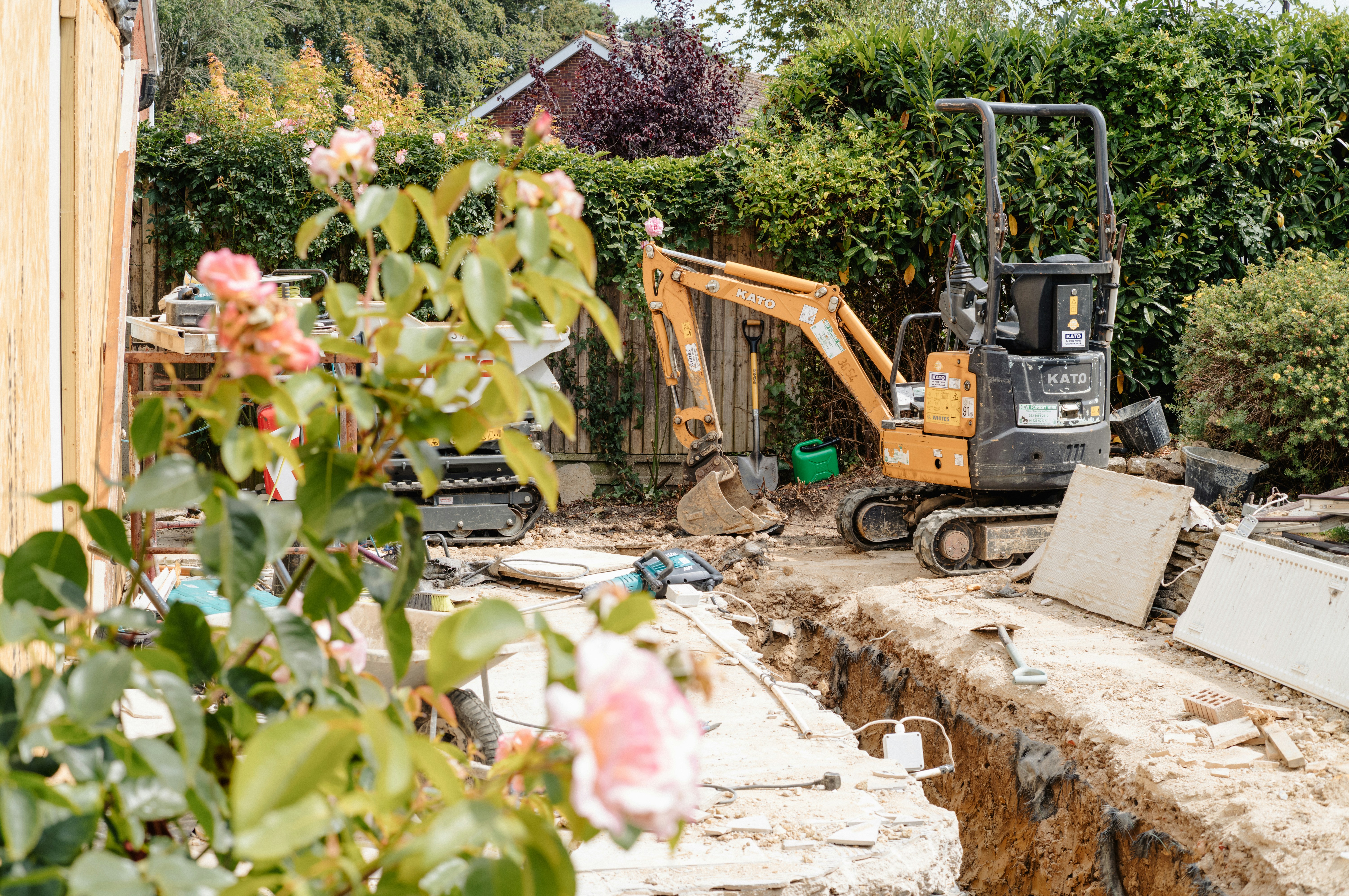 A mini excavator digging a trench in a garden, the kind of digging done for sewer line replacement