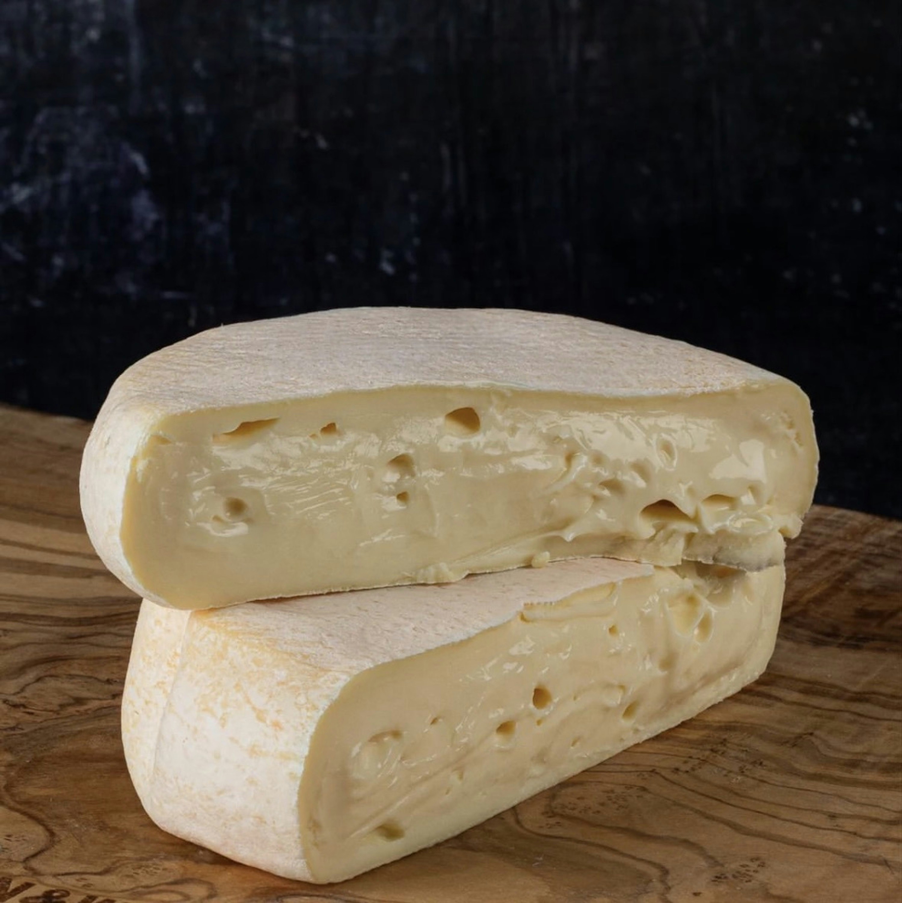 Soft-Ripened Cheese - Two stacked cheese halves on a rustic wooden board.