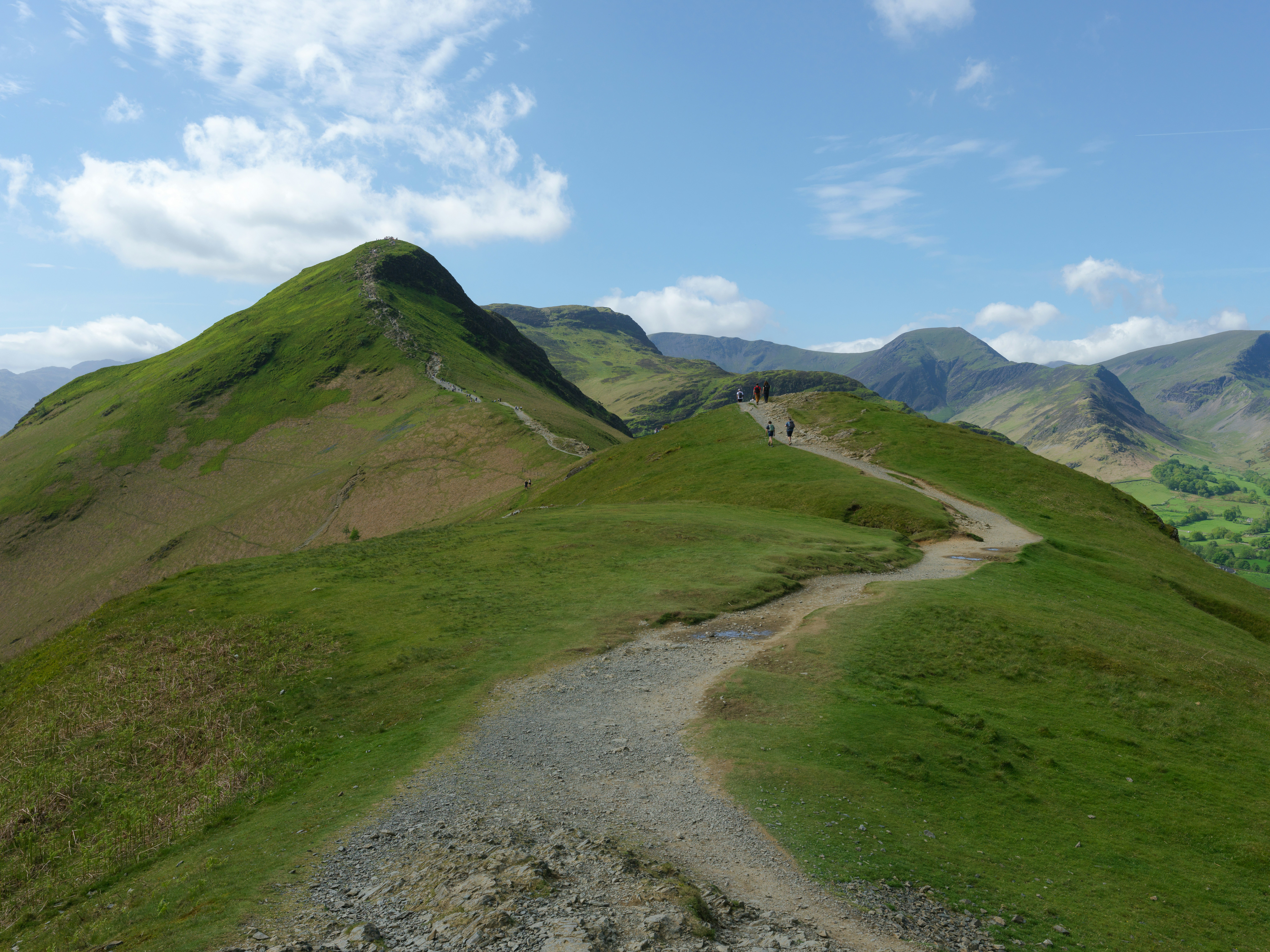 Winding path on a green mountain ridge under blue sky.