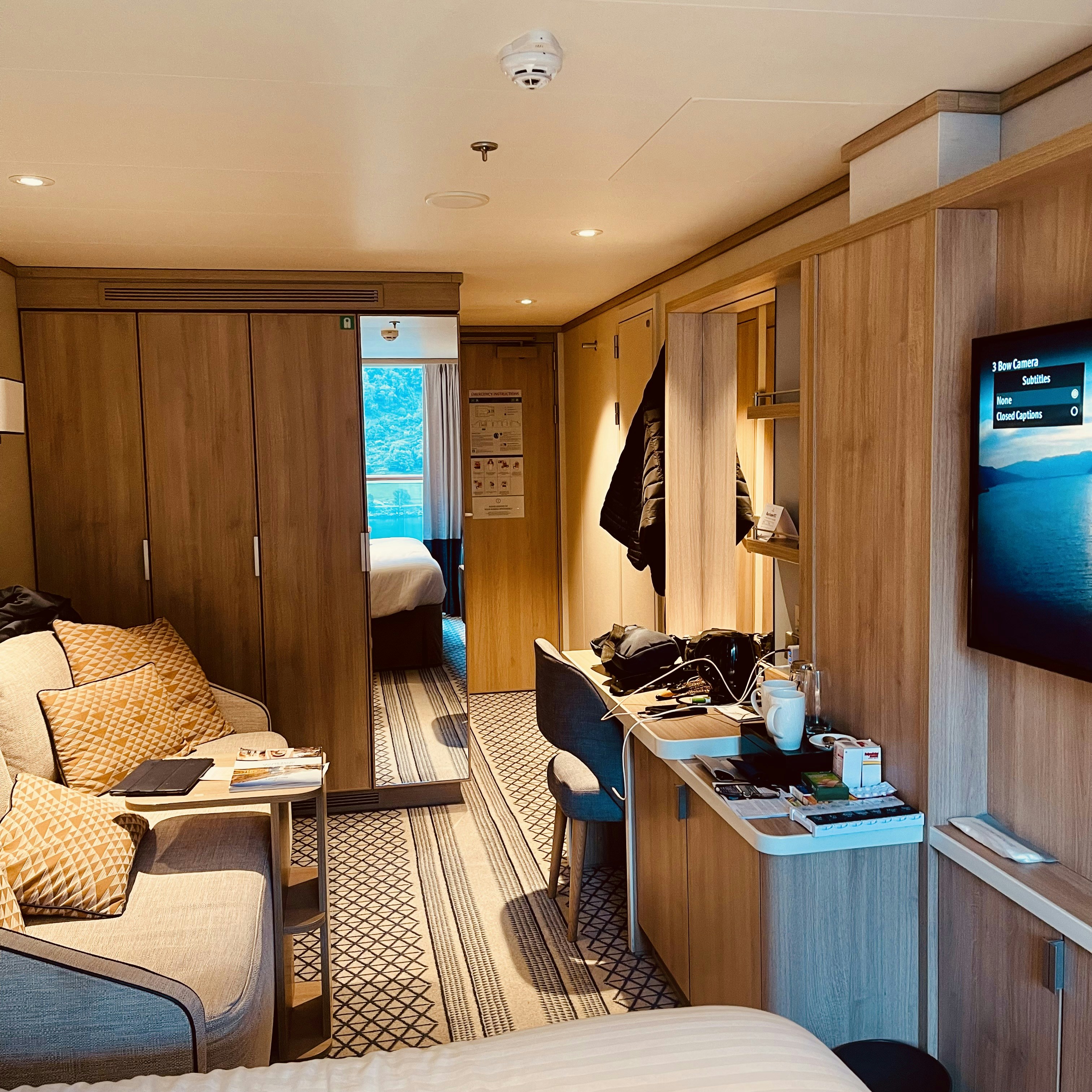 Cabine moderne de paquebot de croisière avec canapé, bureau et télévision.