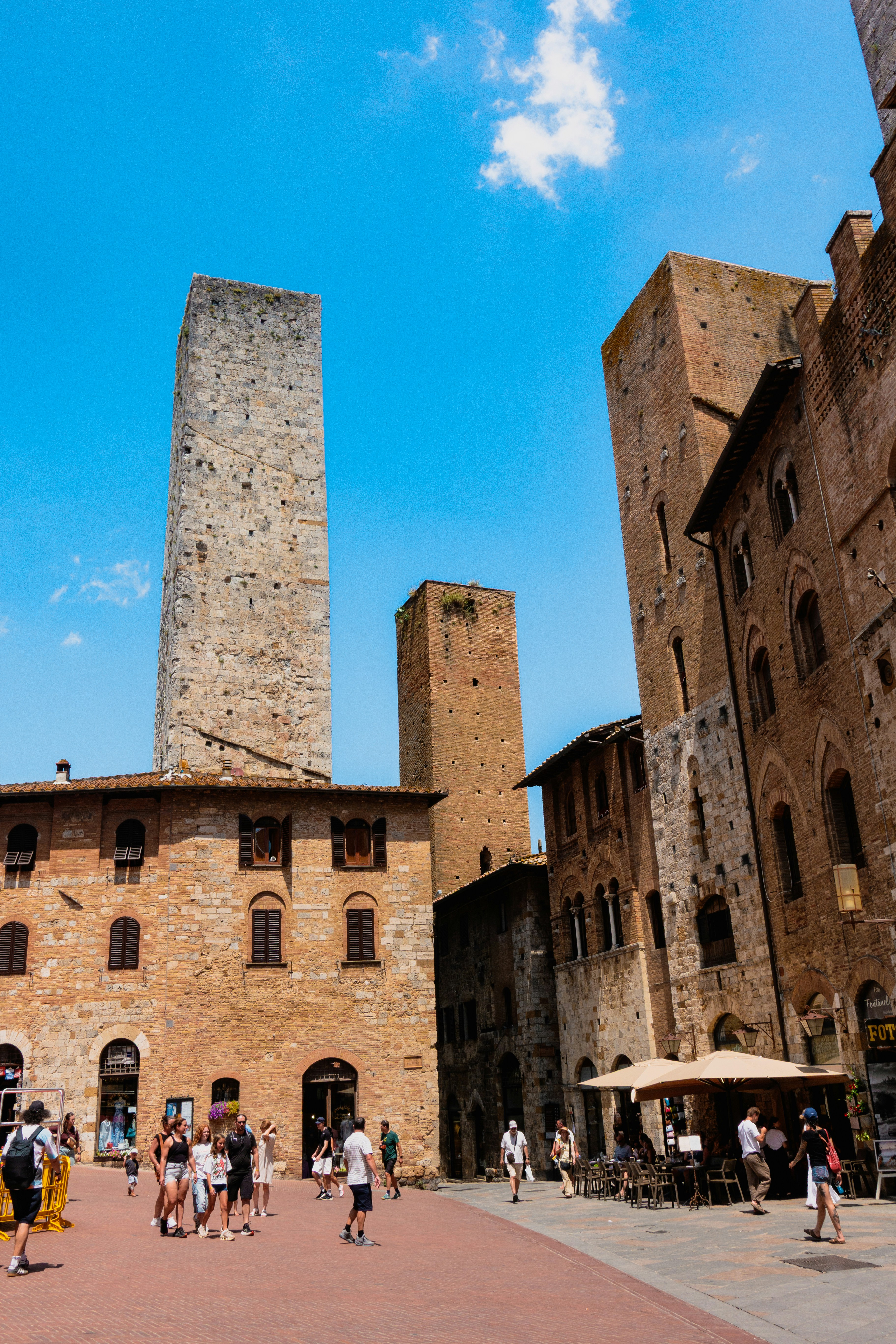 Piazza medievale con torri in pietra e passanti a San Gimignano, Toscana