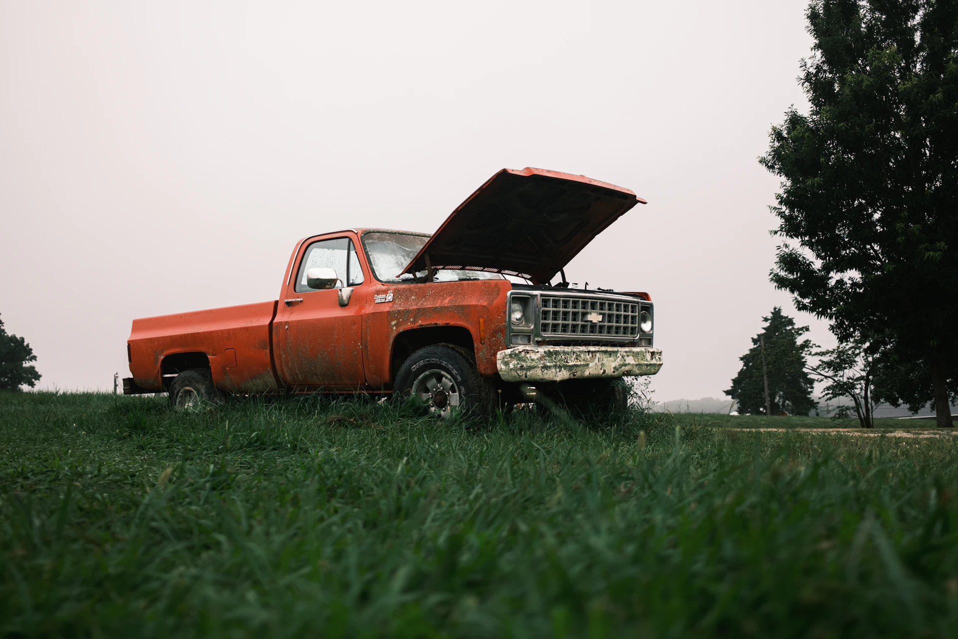 Rusty orange pickup truck with hood open in a field