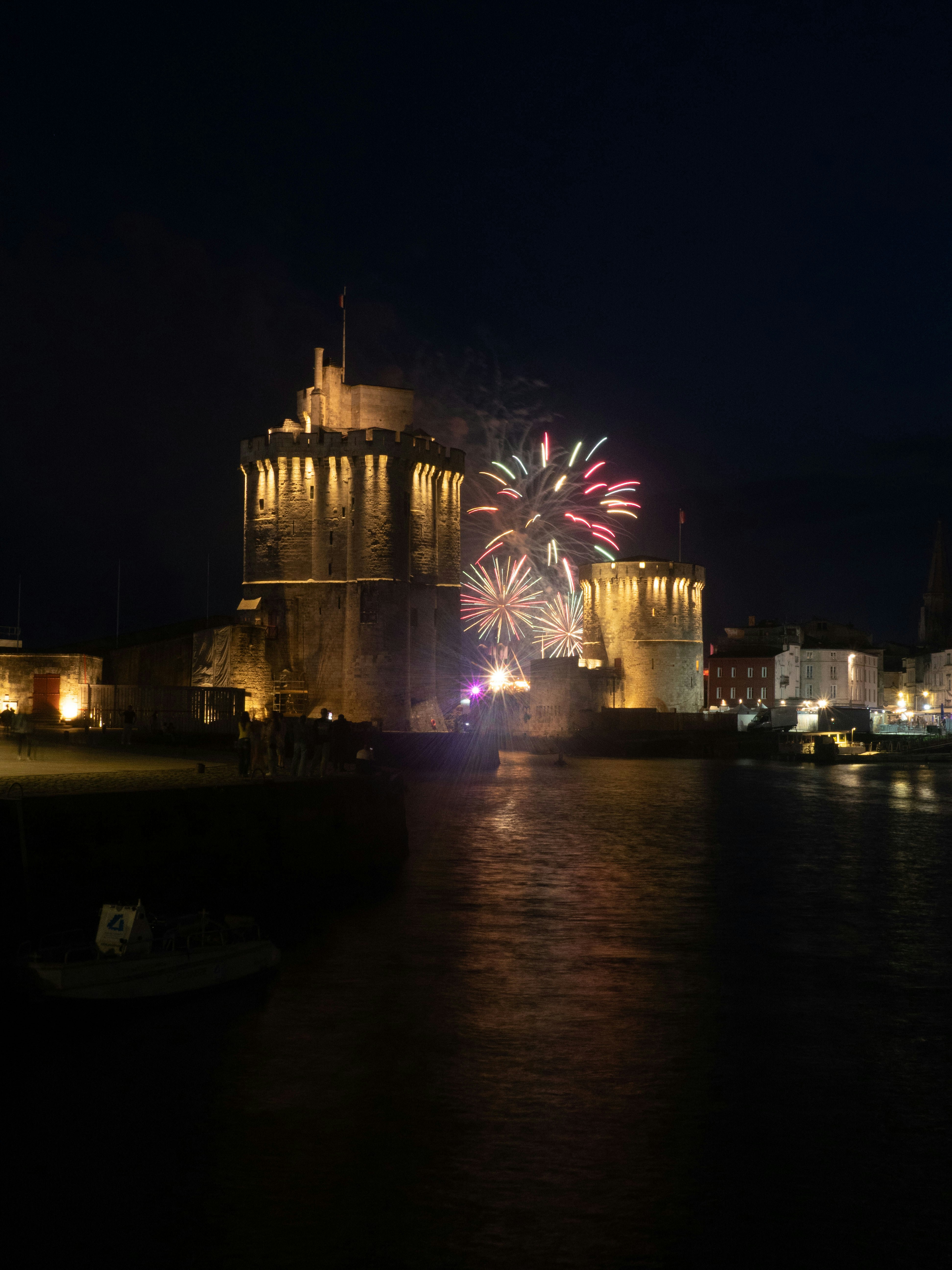 Fireworks explode over an illuminated historic fortress at night.