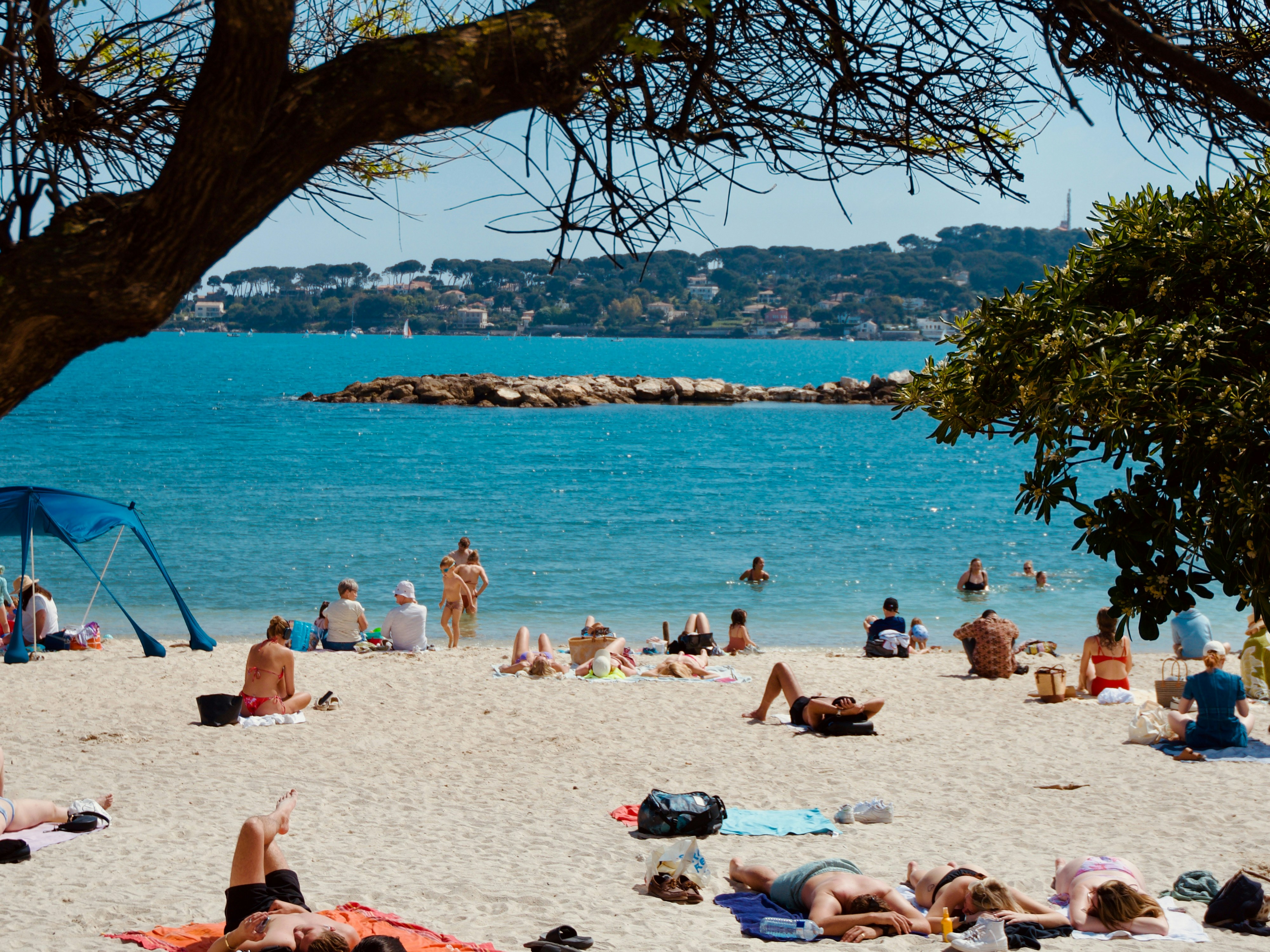 People relaxing on a sunny beach with clear blue water.