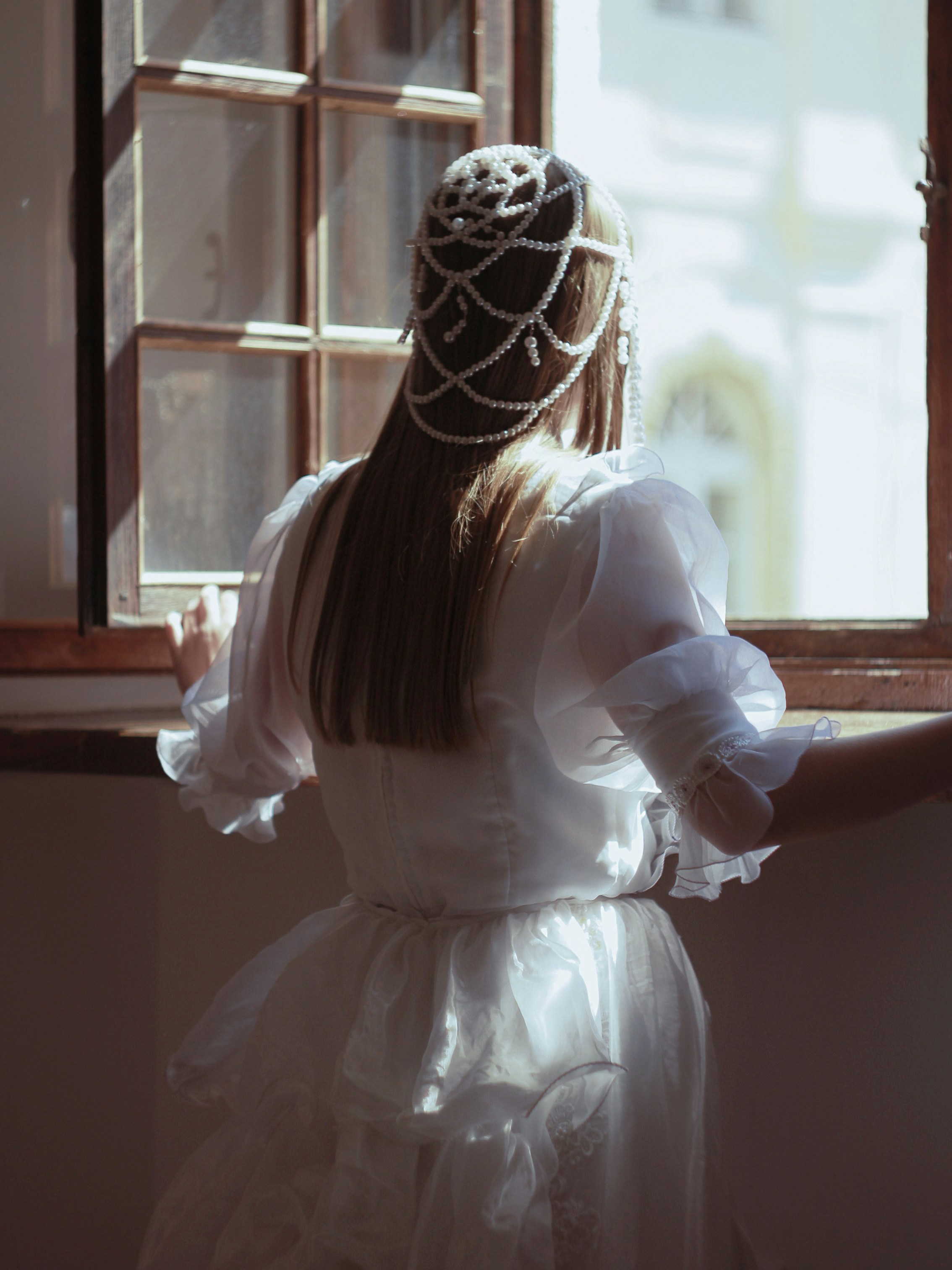 Woman in white dress and pearl headpiece by window