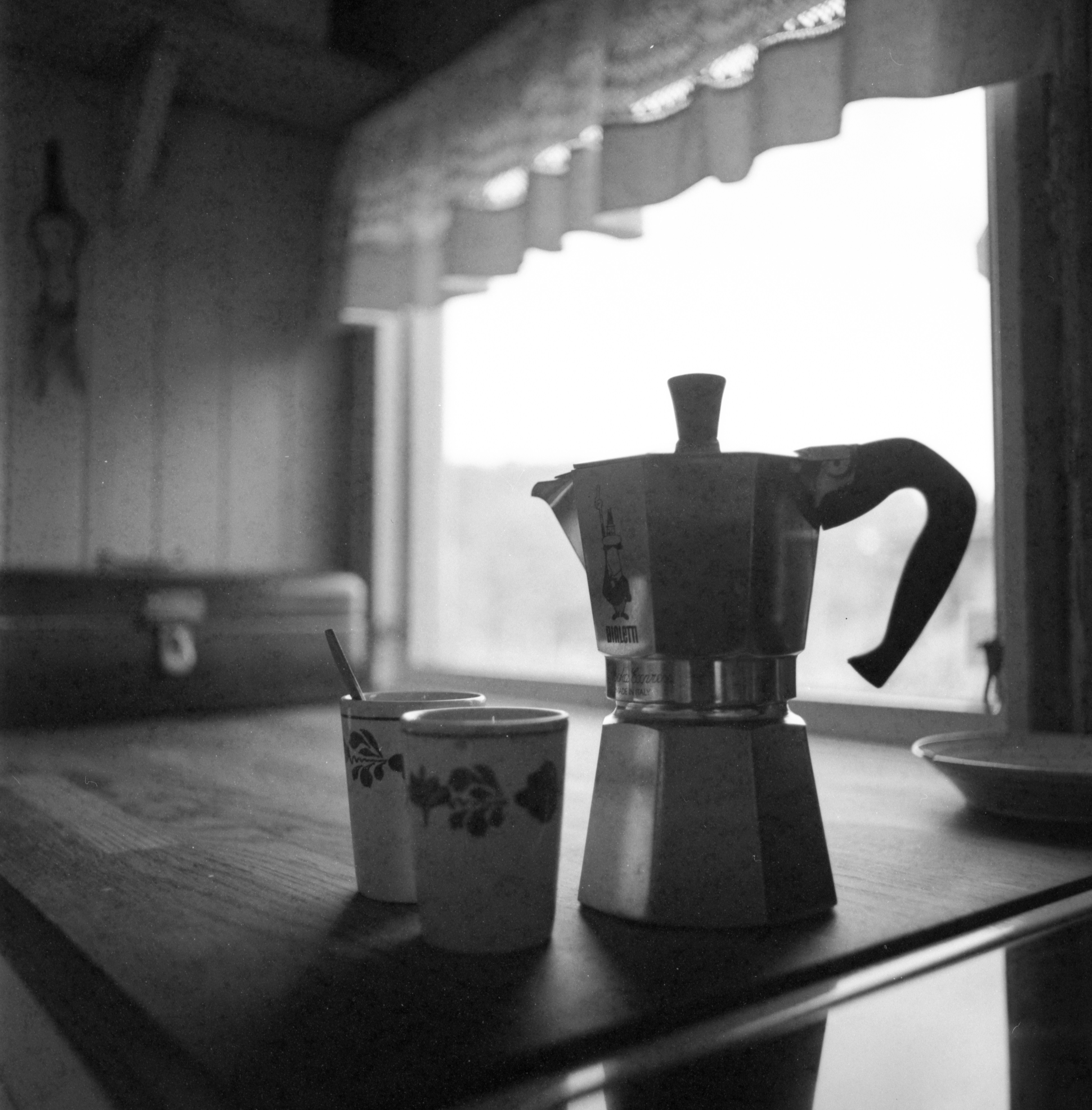 A moka pot and two cups on a wooden table