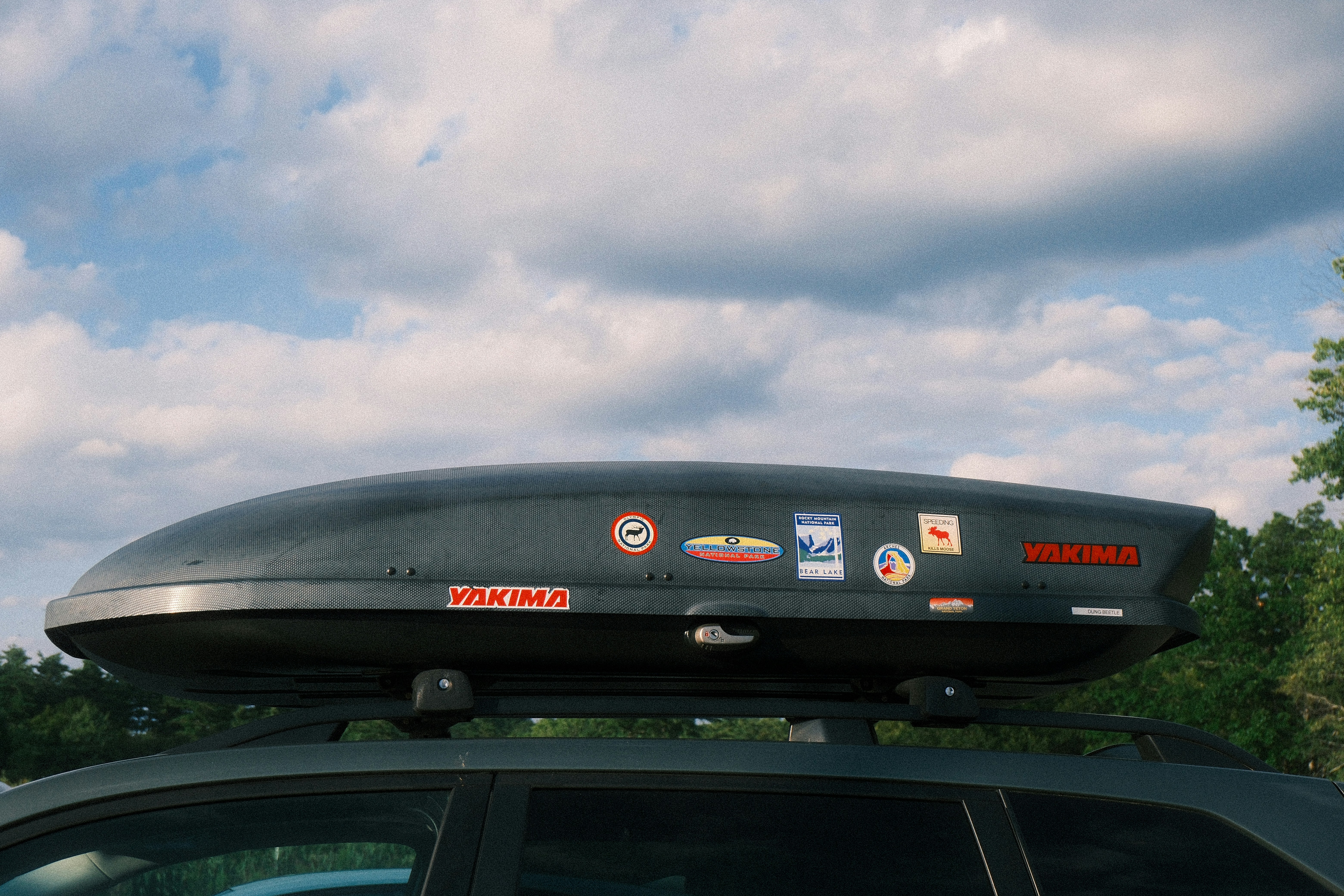 Car roof cargo box with stickers against a cloudy sky