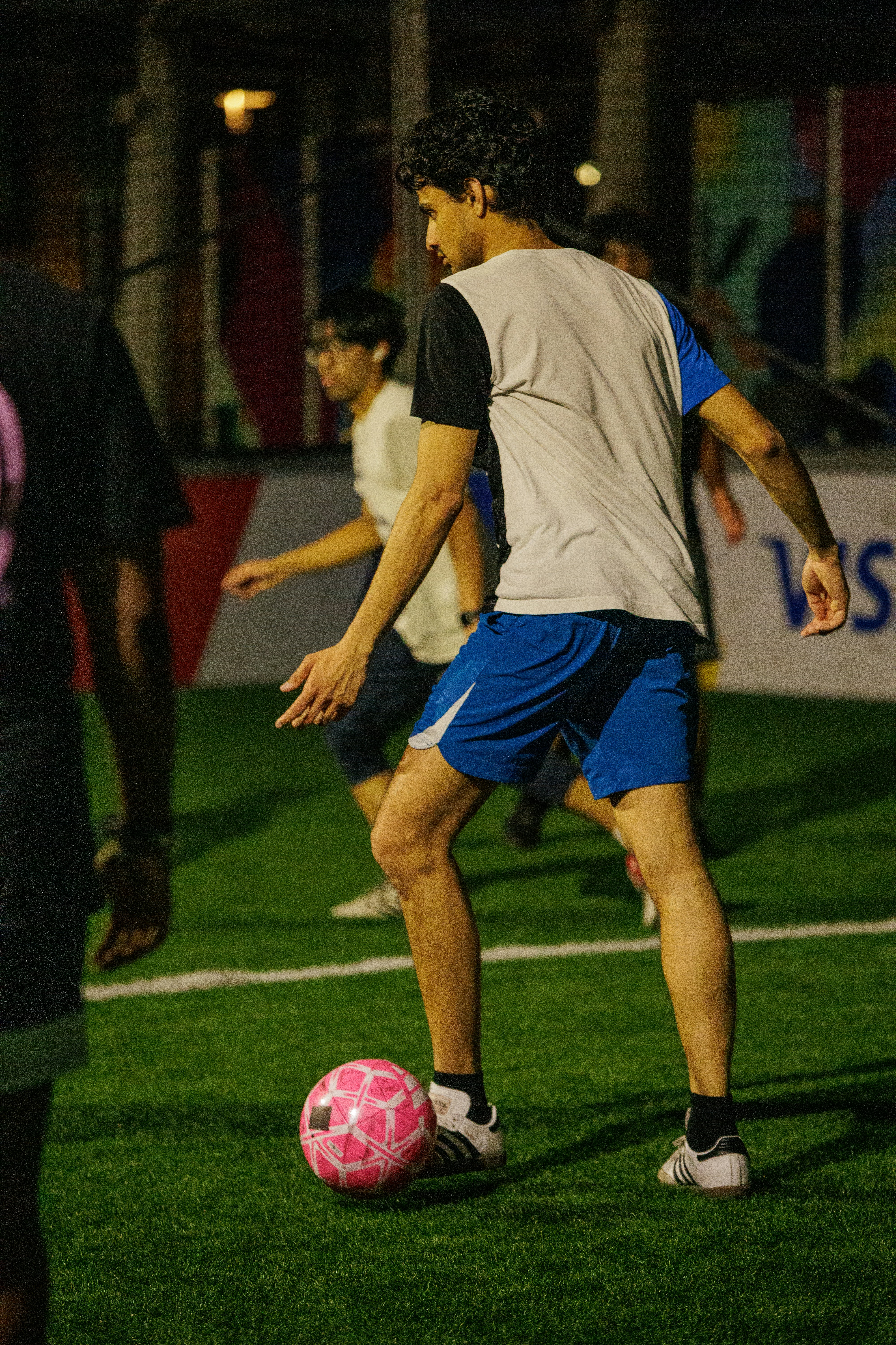 A person dribbling a pink soccer ball on an artificial turf field at night