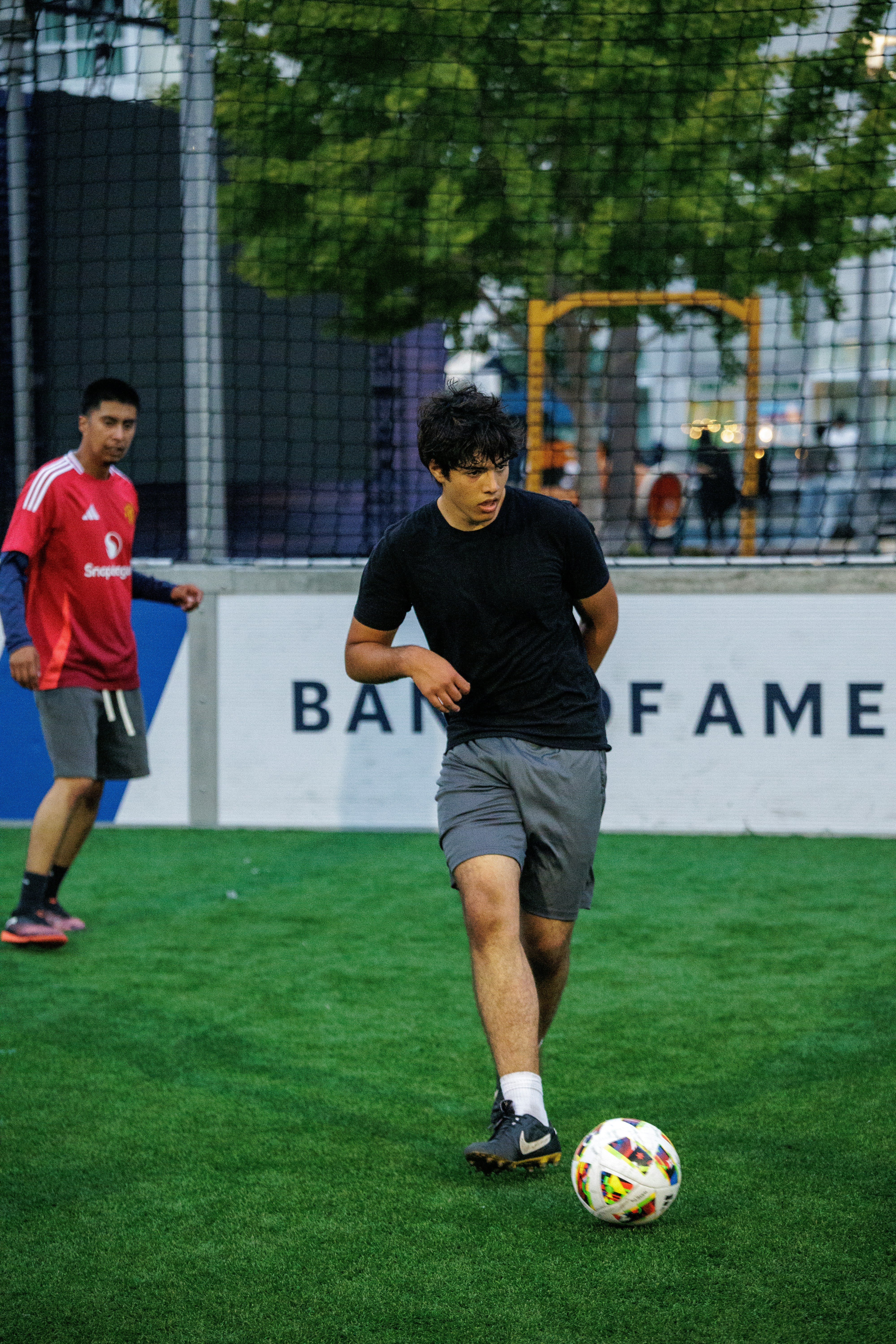 A person in a black t-shirt dribbling a soccer ball on an artificial turf field