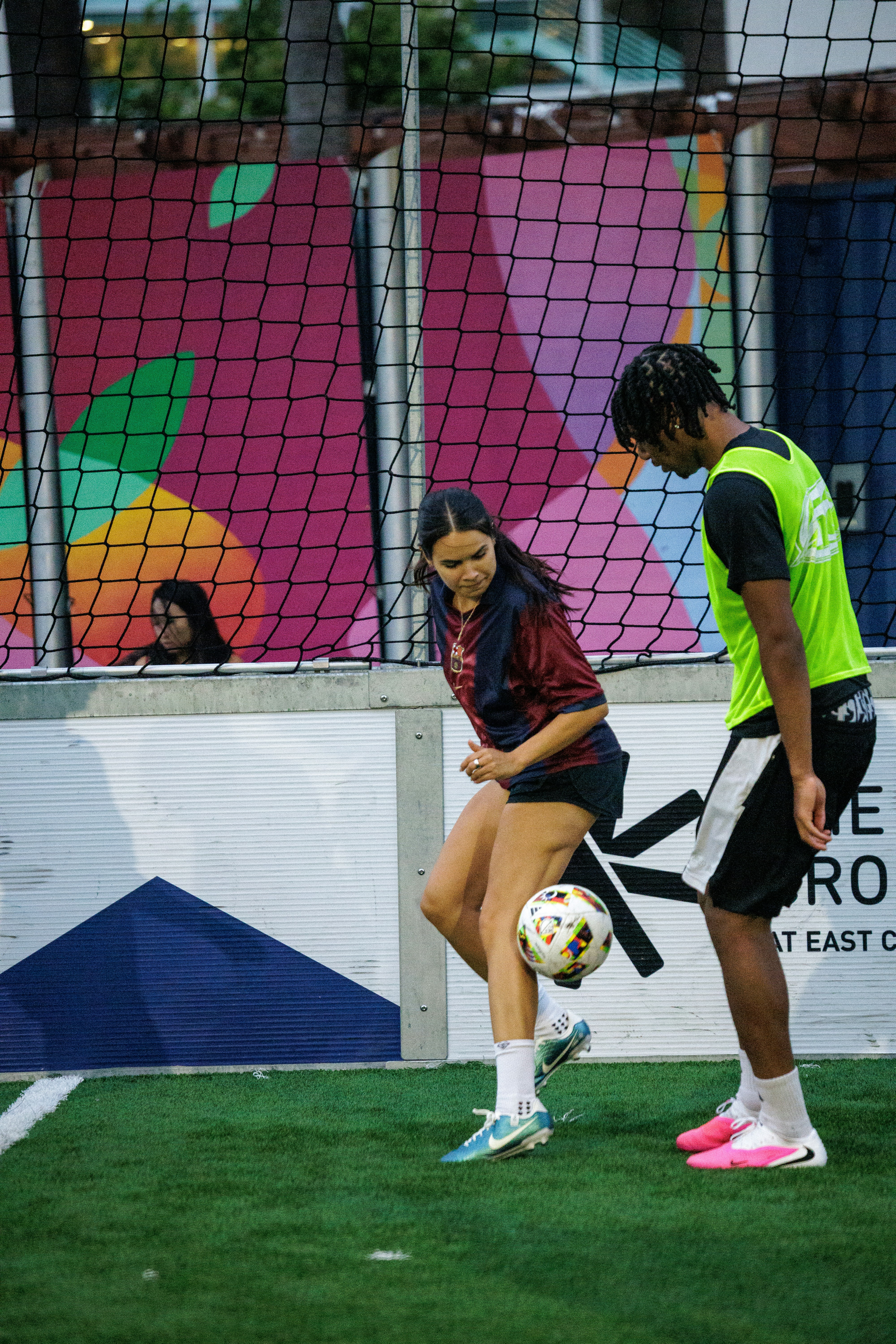 A woman controlling a soccer ball with her knee near a man on a pitch