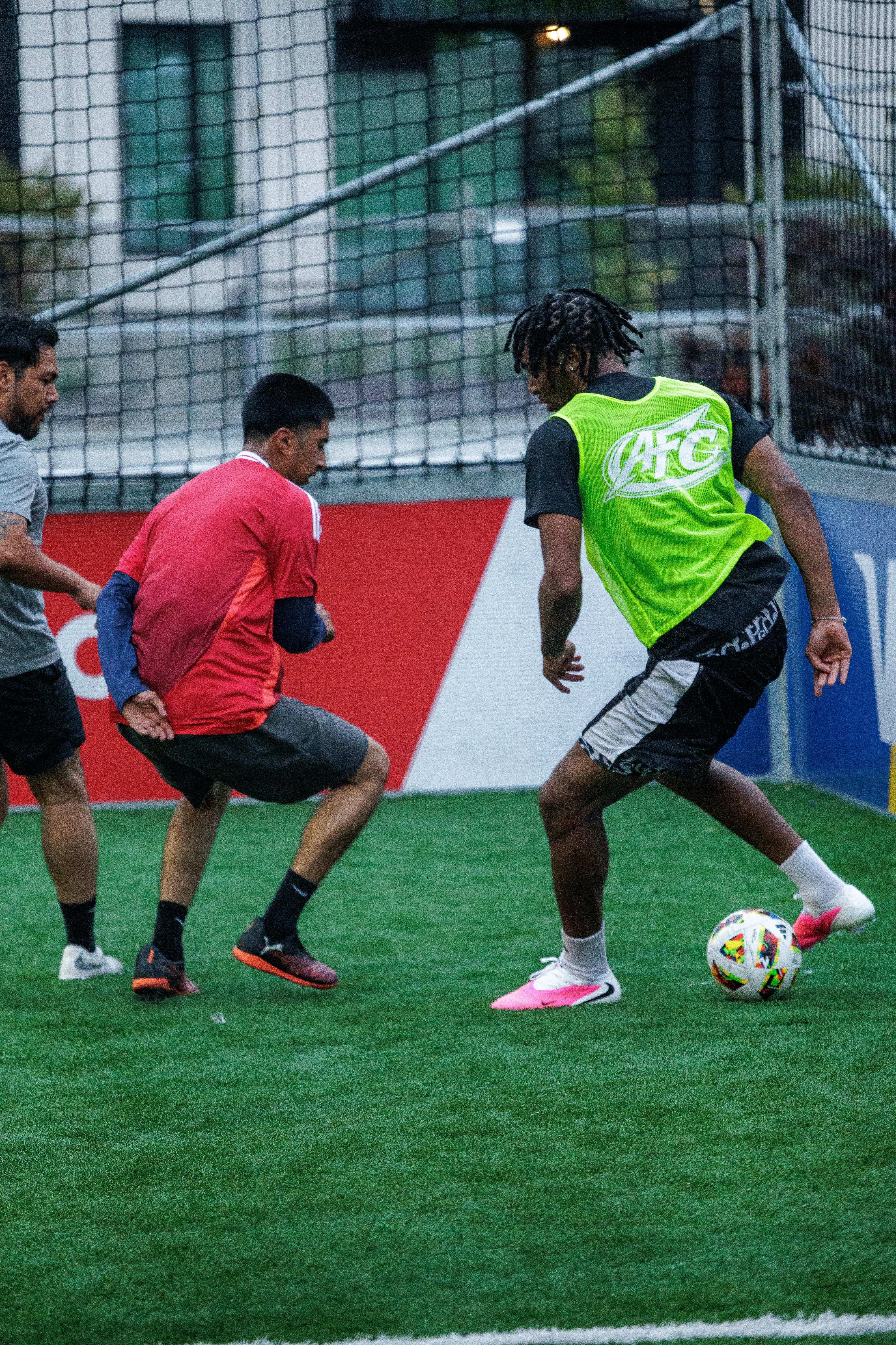 Three people playing soccer on an artificial turf field with a net