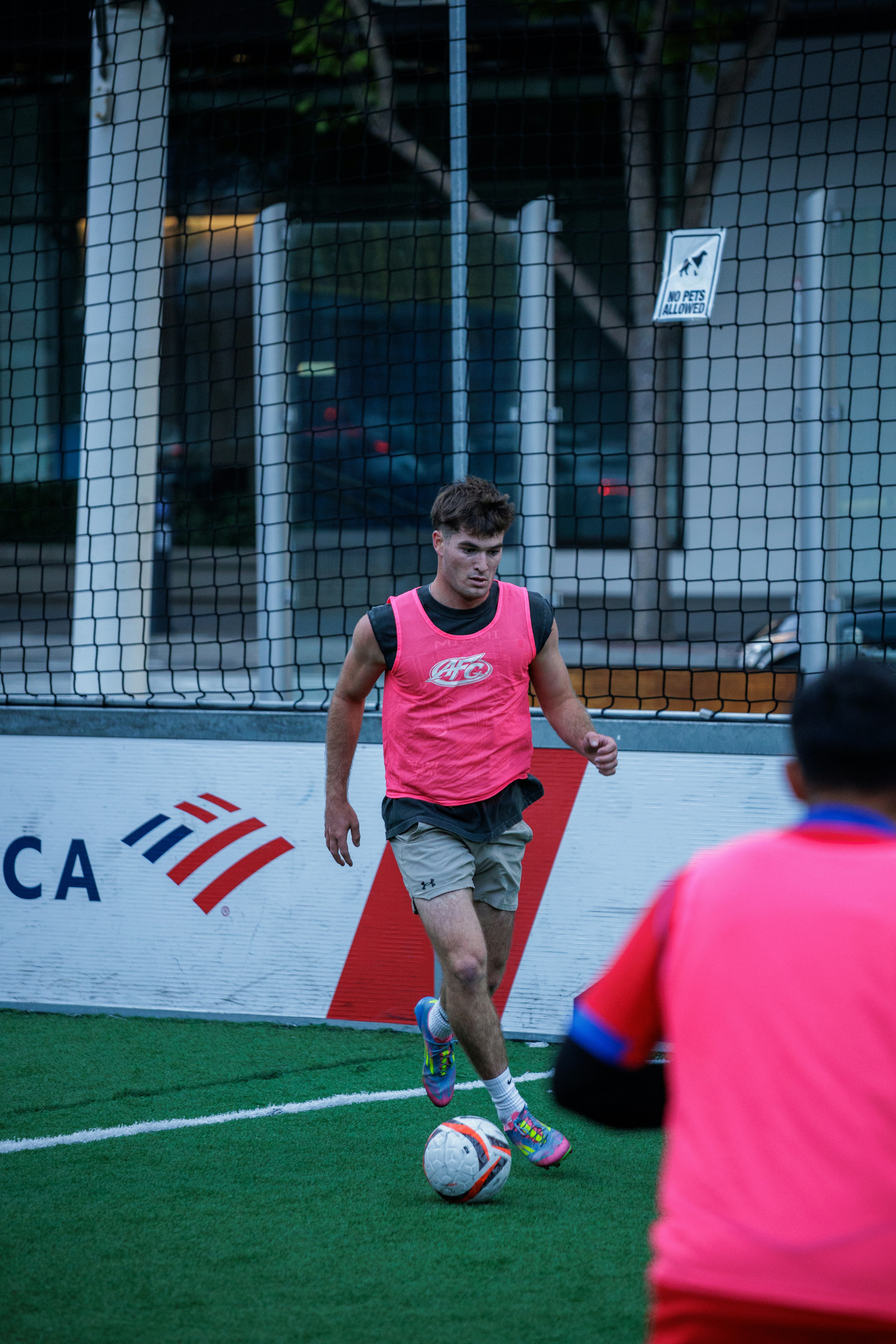 A man in a pink training bib dribbling a soccer ball on a field