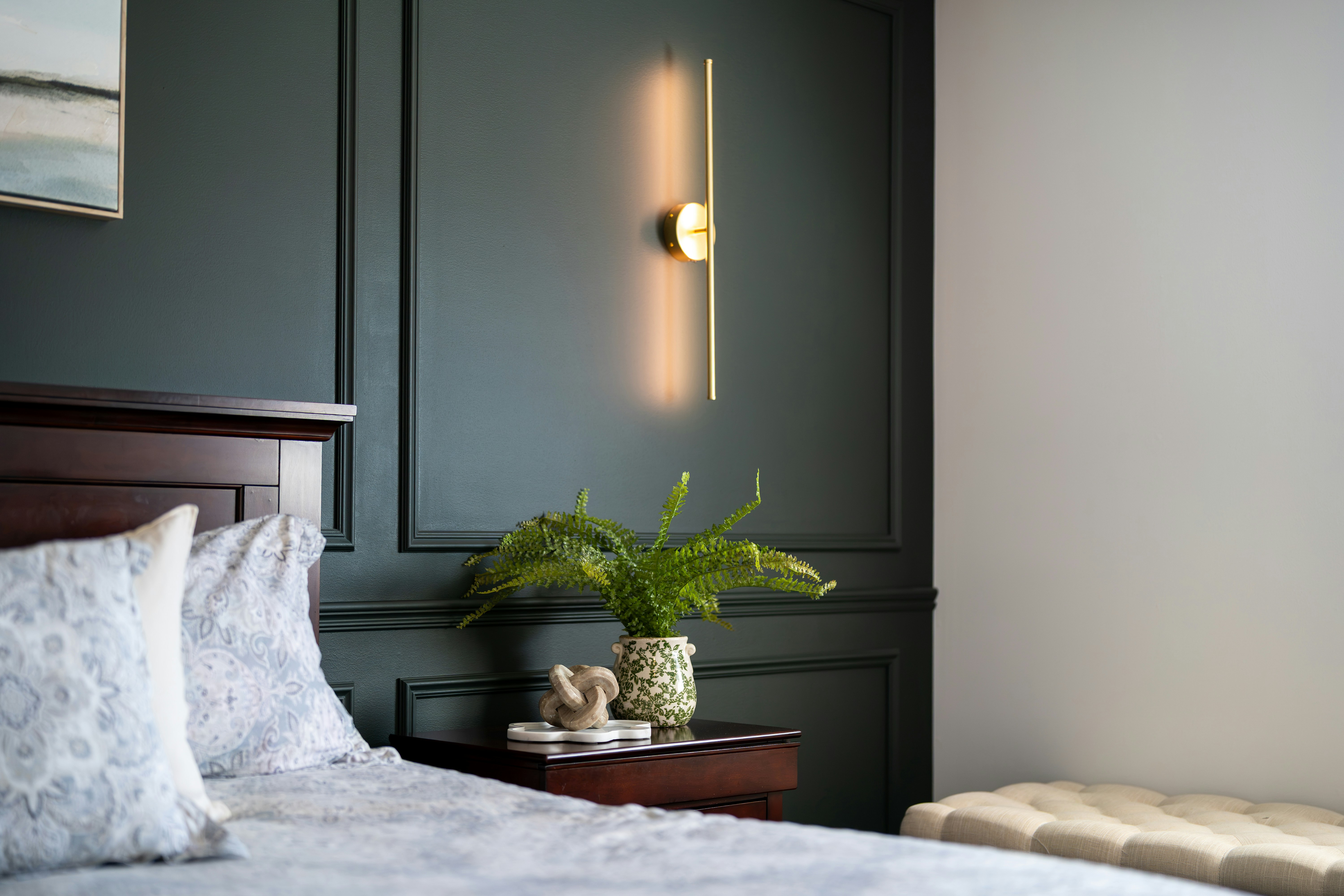 Modern bedroom with dark green wall, stylish light, and plant.