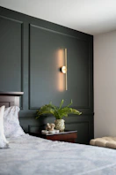 Modern bedroom with dark green wainscoting, illuminated sconce, and fern