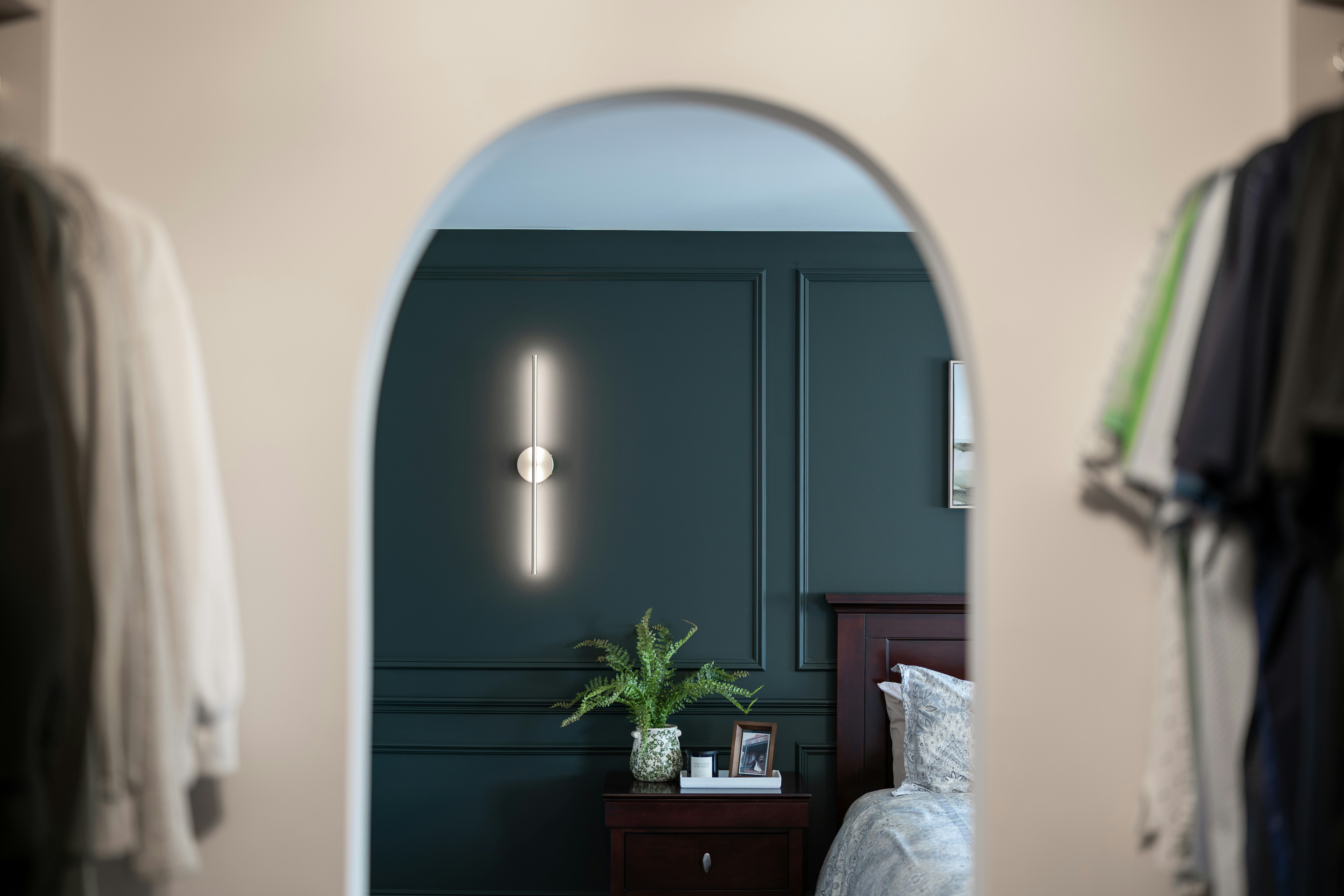 Dark green bedroom with modern light viewed through an archway.