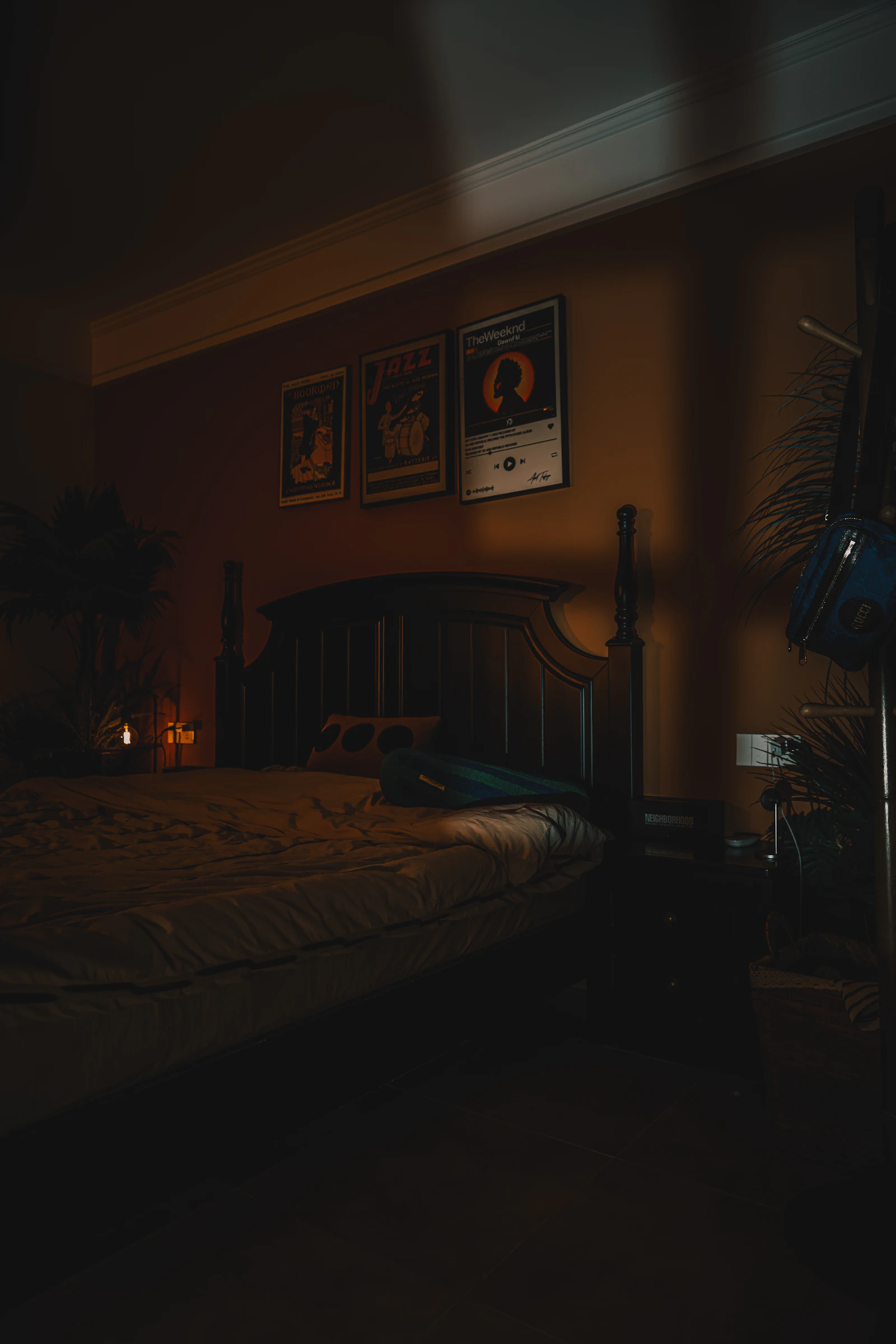 A dark bedroom with posters on the wall and warm lighting