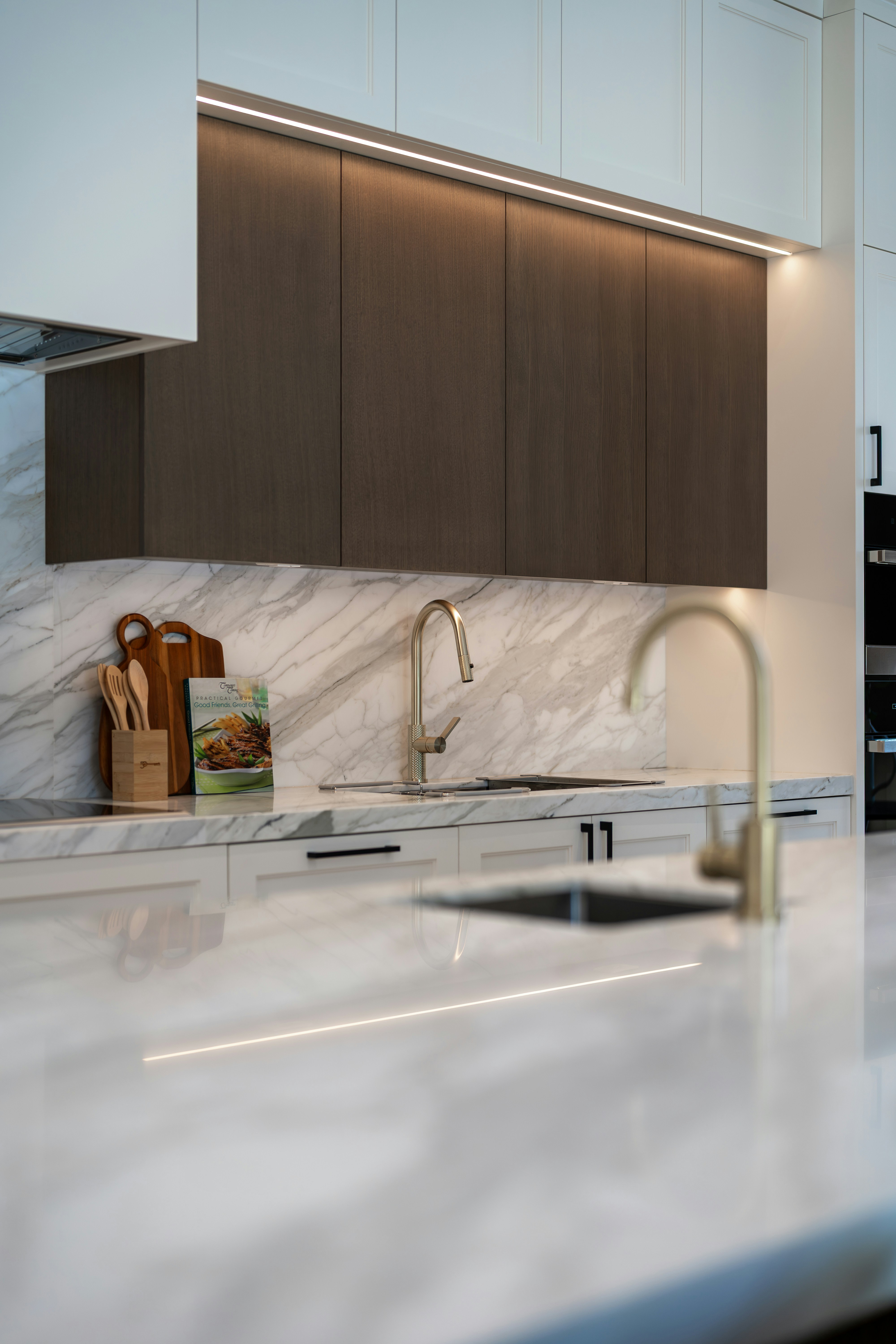 Modern kitchen with marble countertops, dark cabinets, and two sinks.