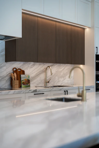 Modern kitchen with marble countertops, dark cabinets vinyl wrapped in oak wood, and two sinks