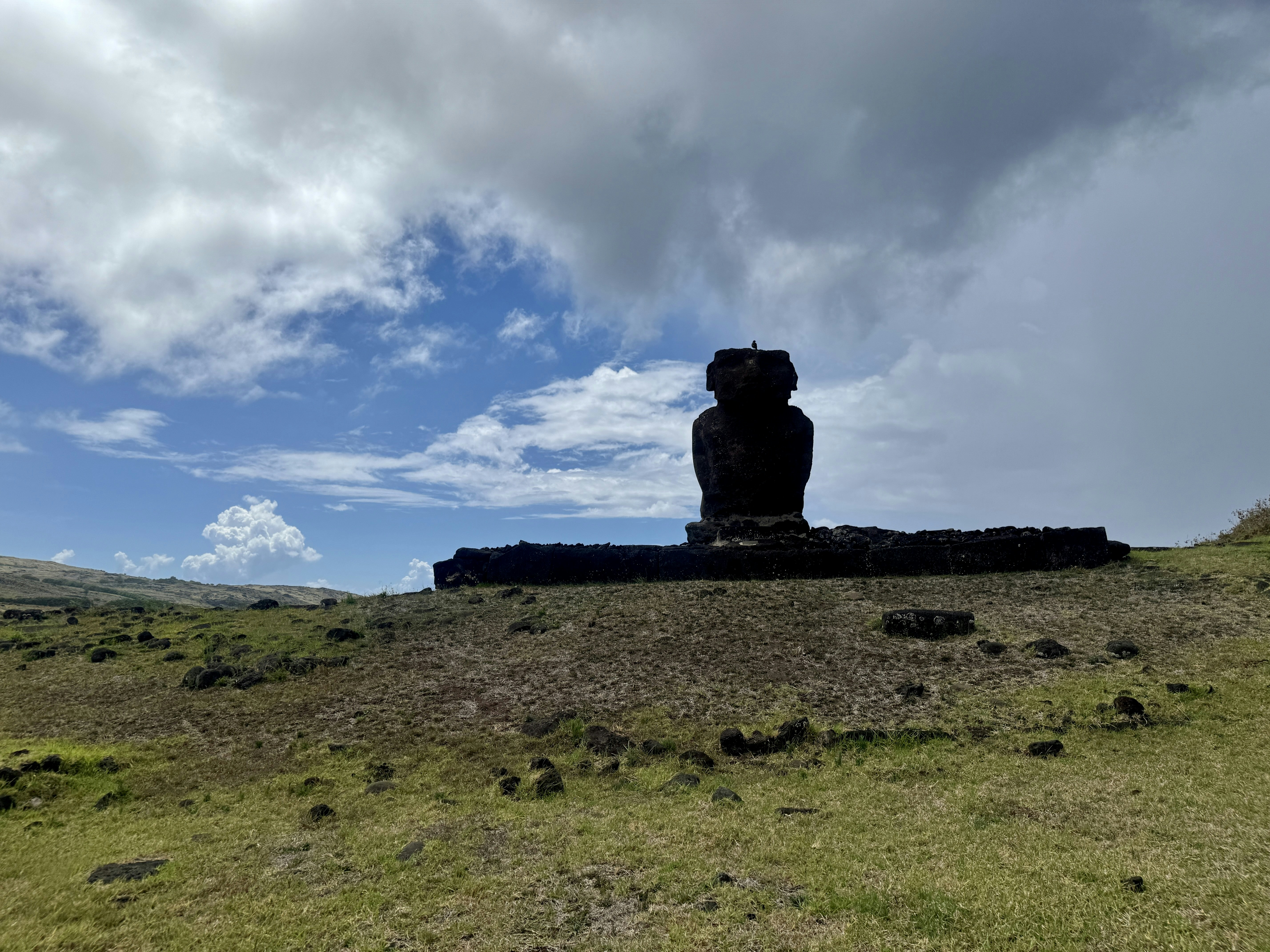 Moai statue on grassy hill under cloudy sky