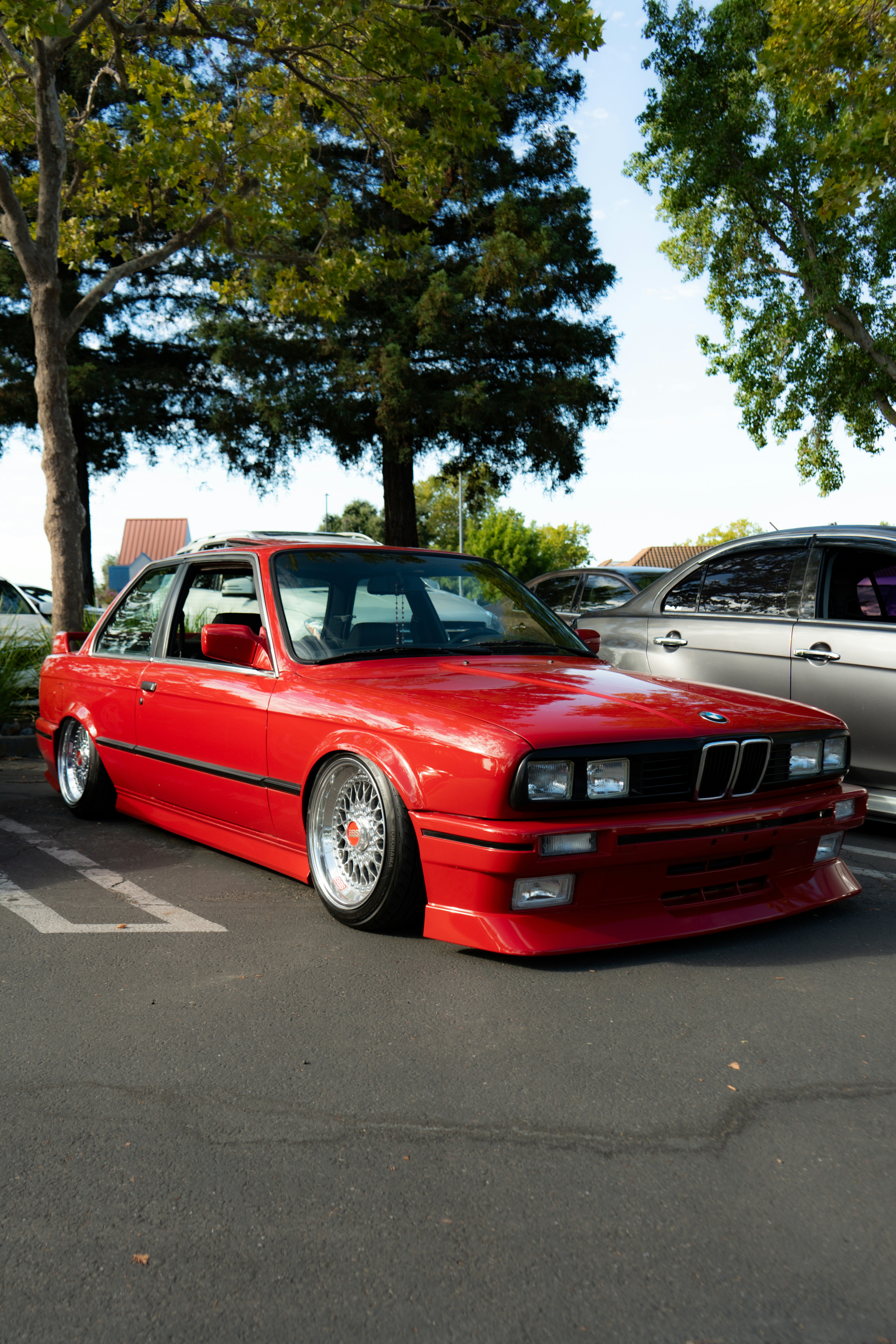 Um elegante BMW e30 vermelho estacionado sob árvores