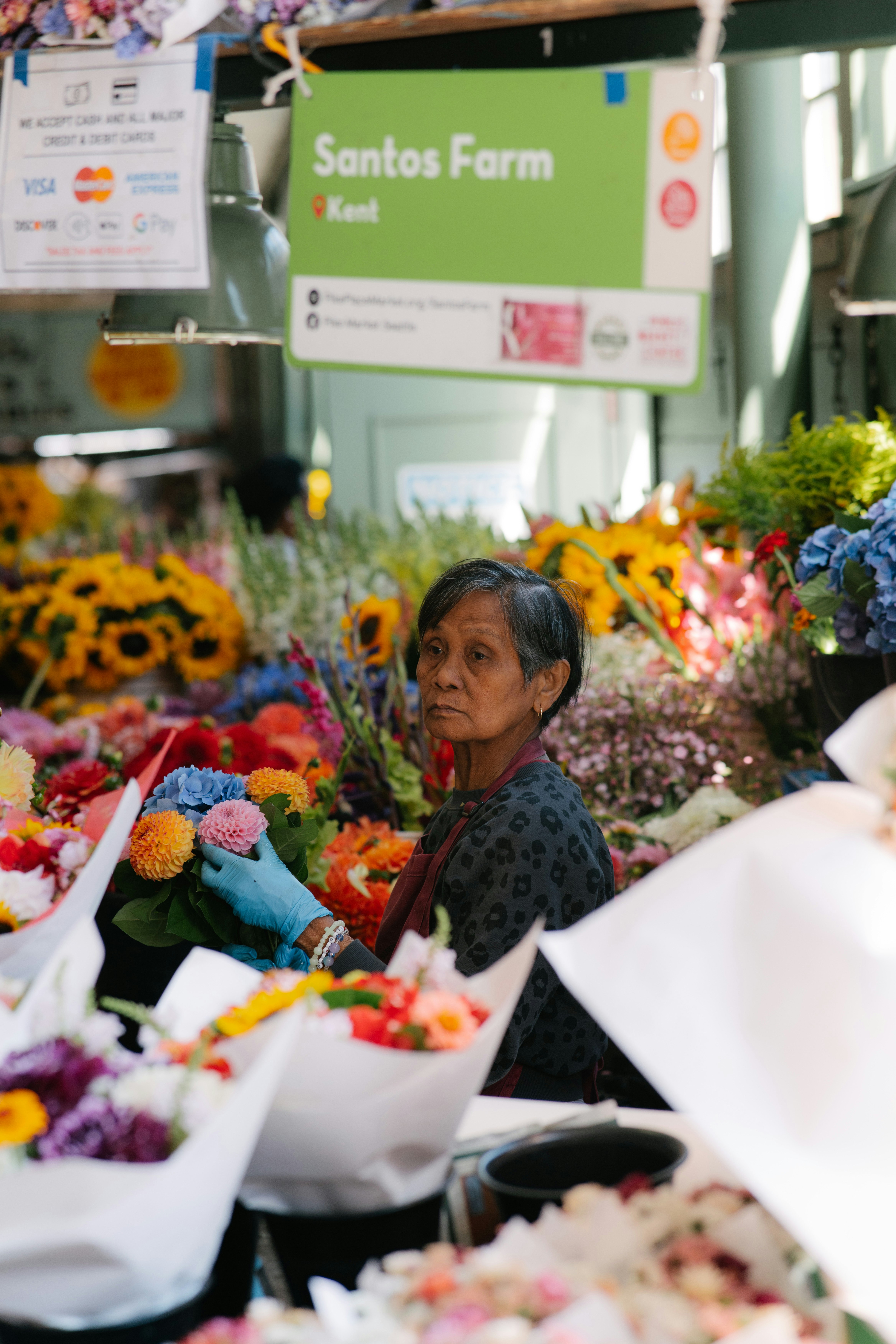 An elderly woman arranging colorful flowers at a market stall