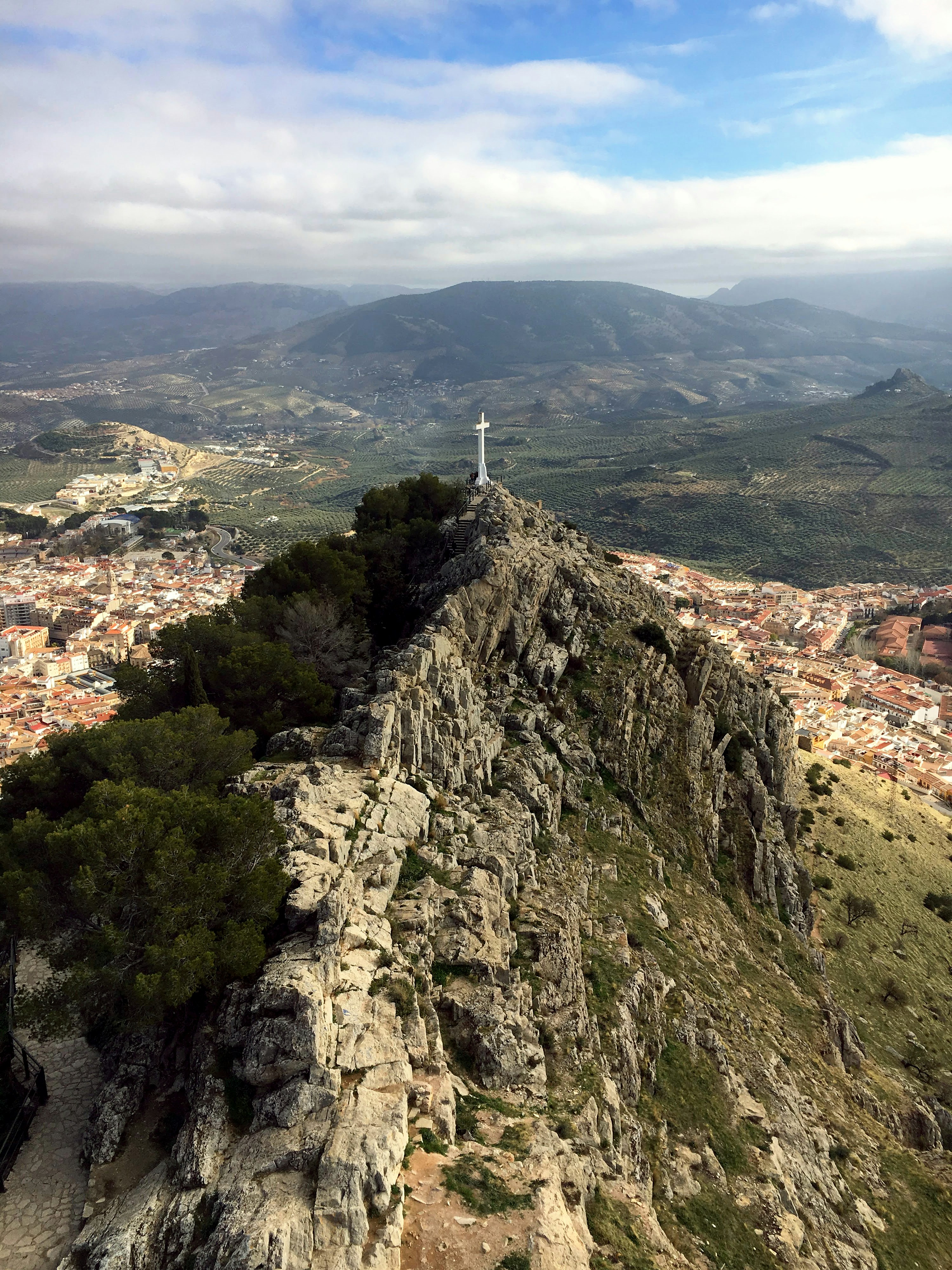 White cross on a rocky mountain peak above a town